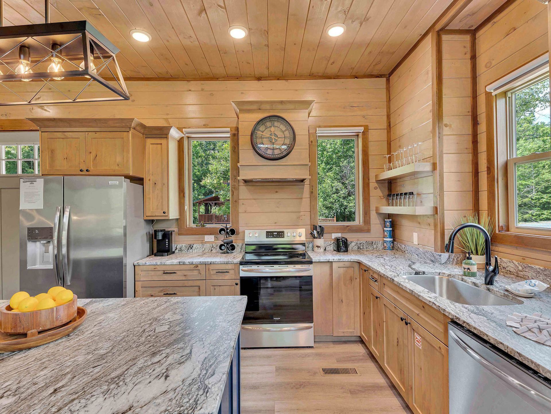 Kitchen with wood paneling, granite countertops, stainless steel appliances, and a large clock.