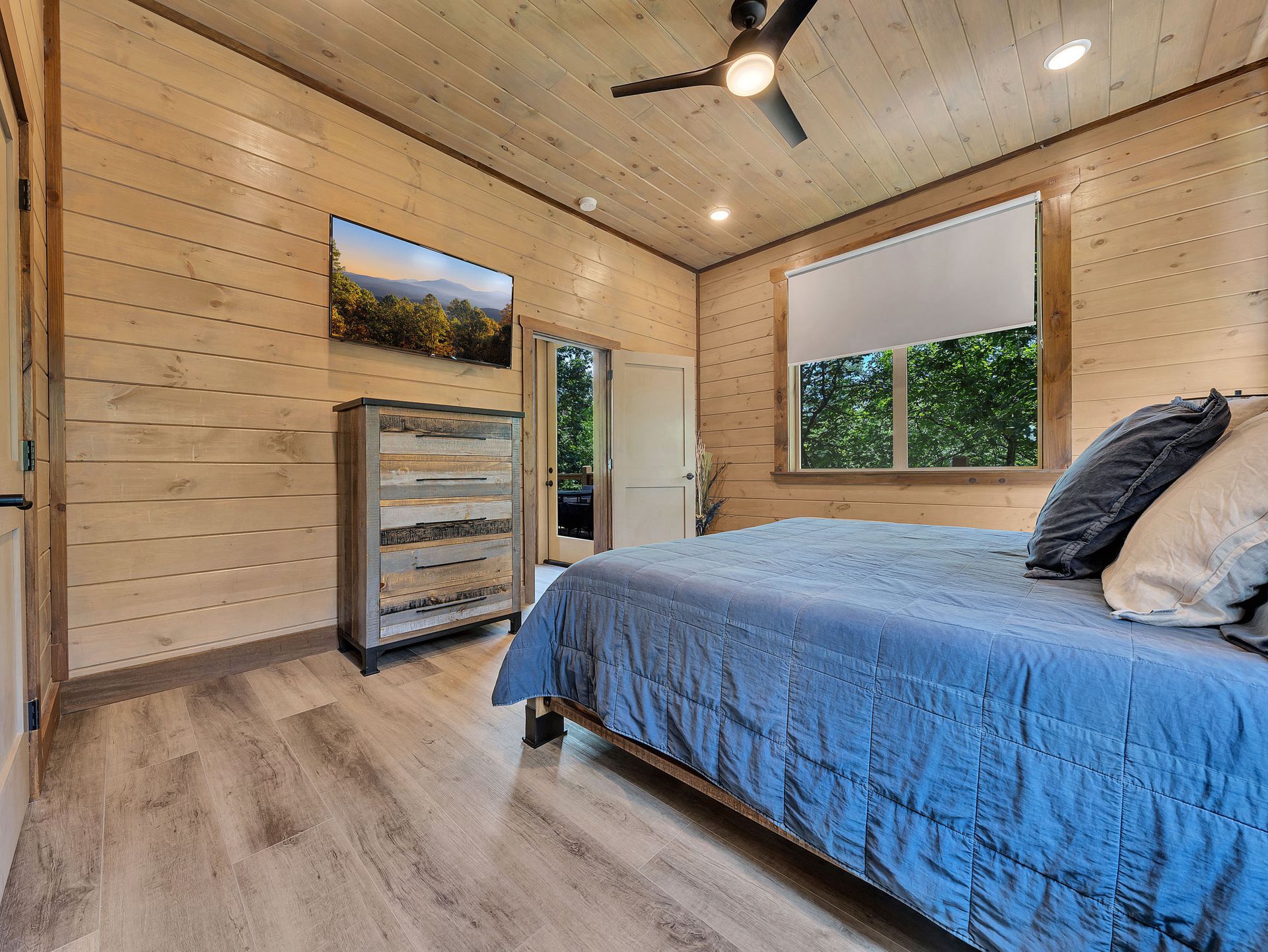 Bedroom with wood paneling, a bed with blue bedding, dresser, and door to the outside.