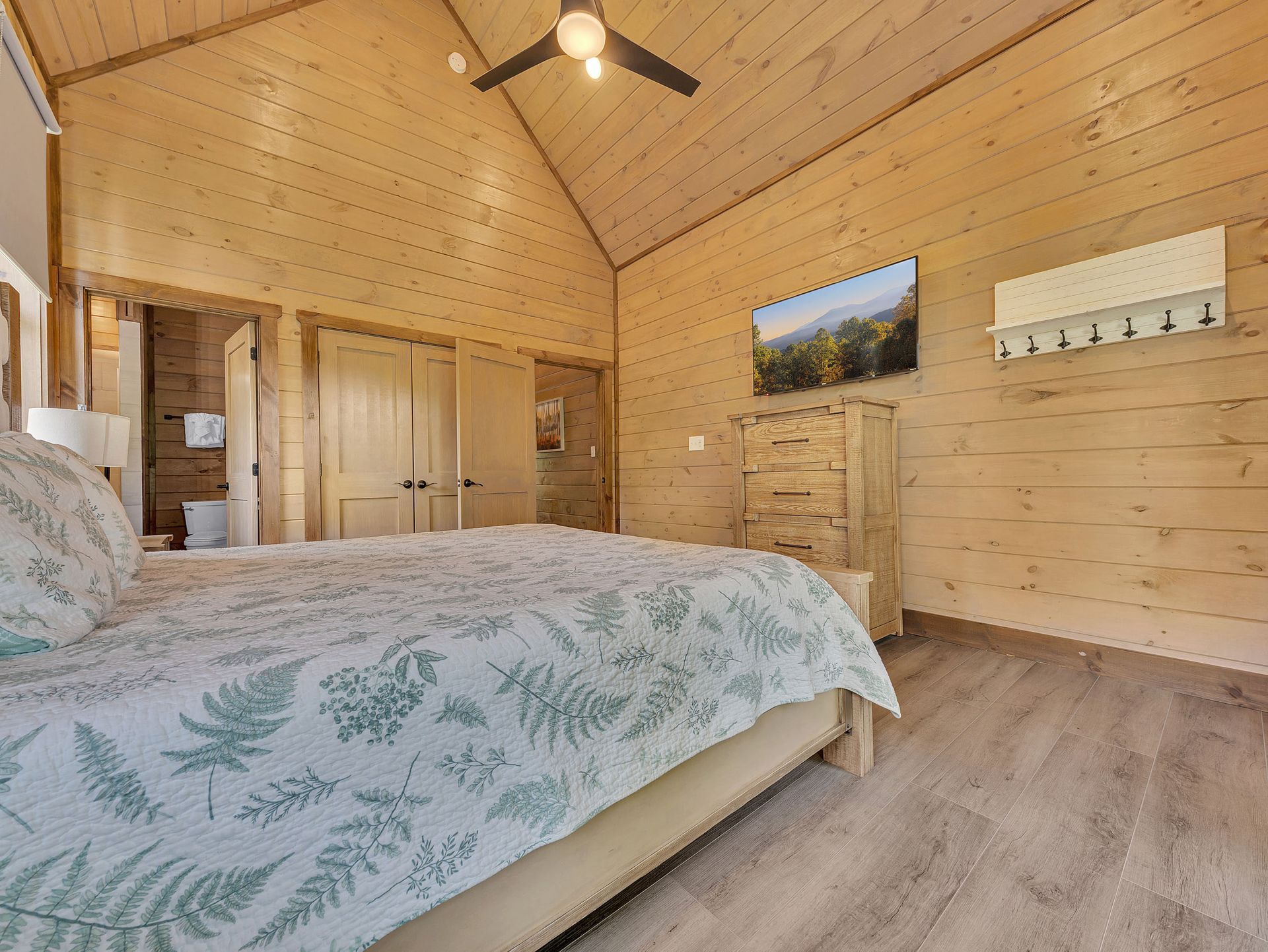 Bedroom with light wood paneling, bed with floral linens, and a dresser.