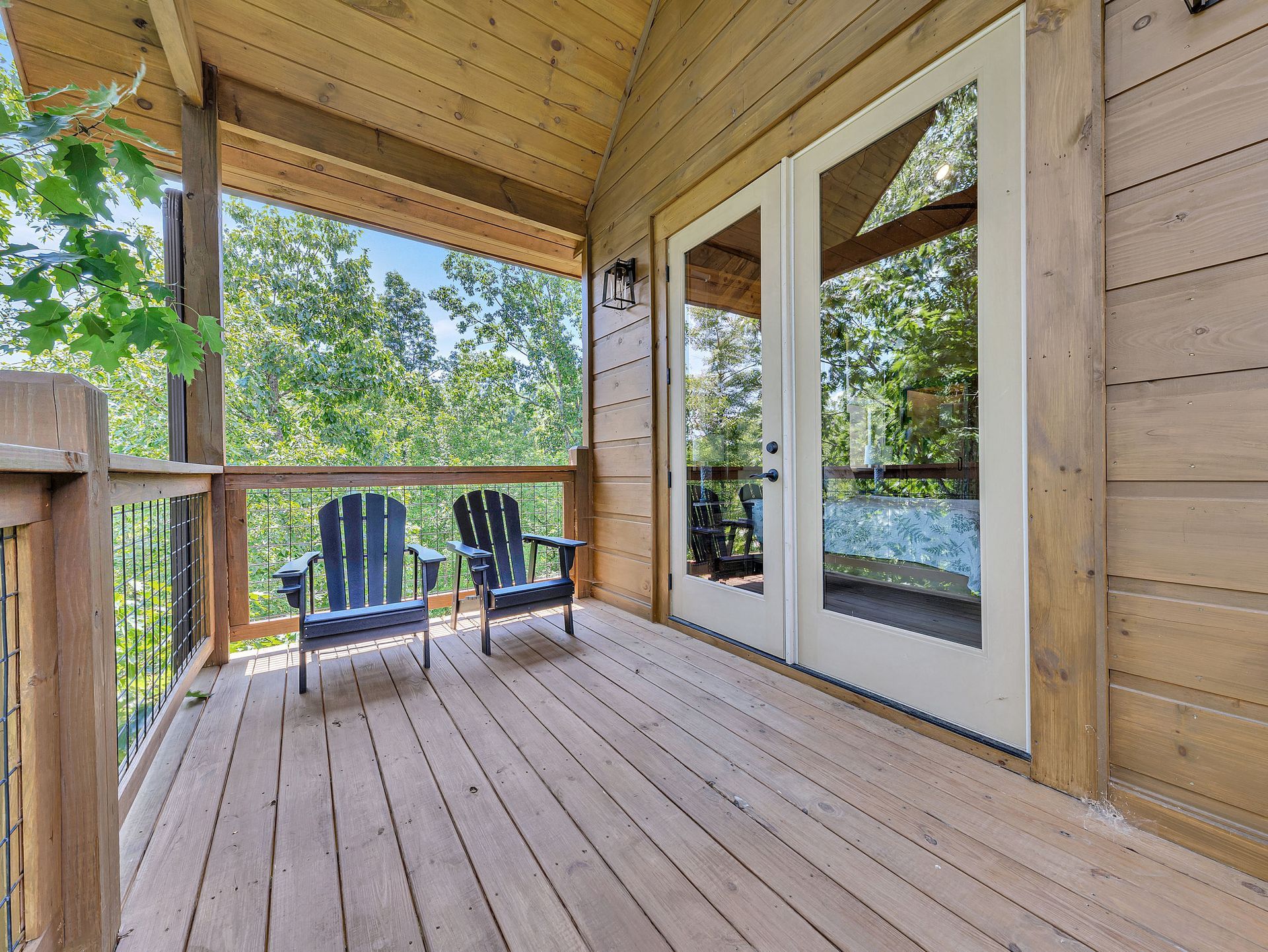 Wooden deck with two chairs, overlooking trees; French doors to the right.