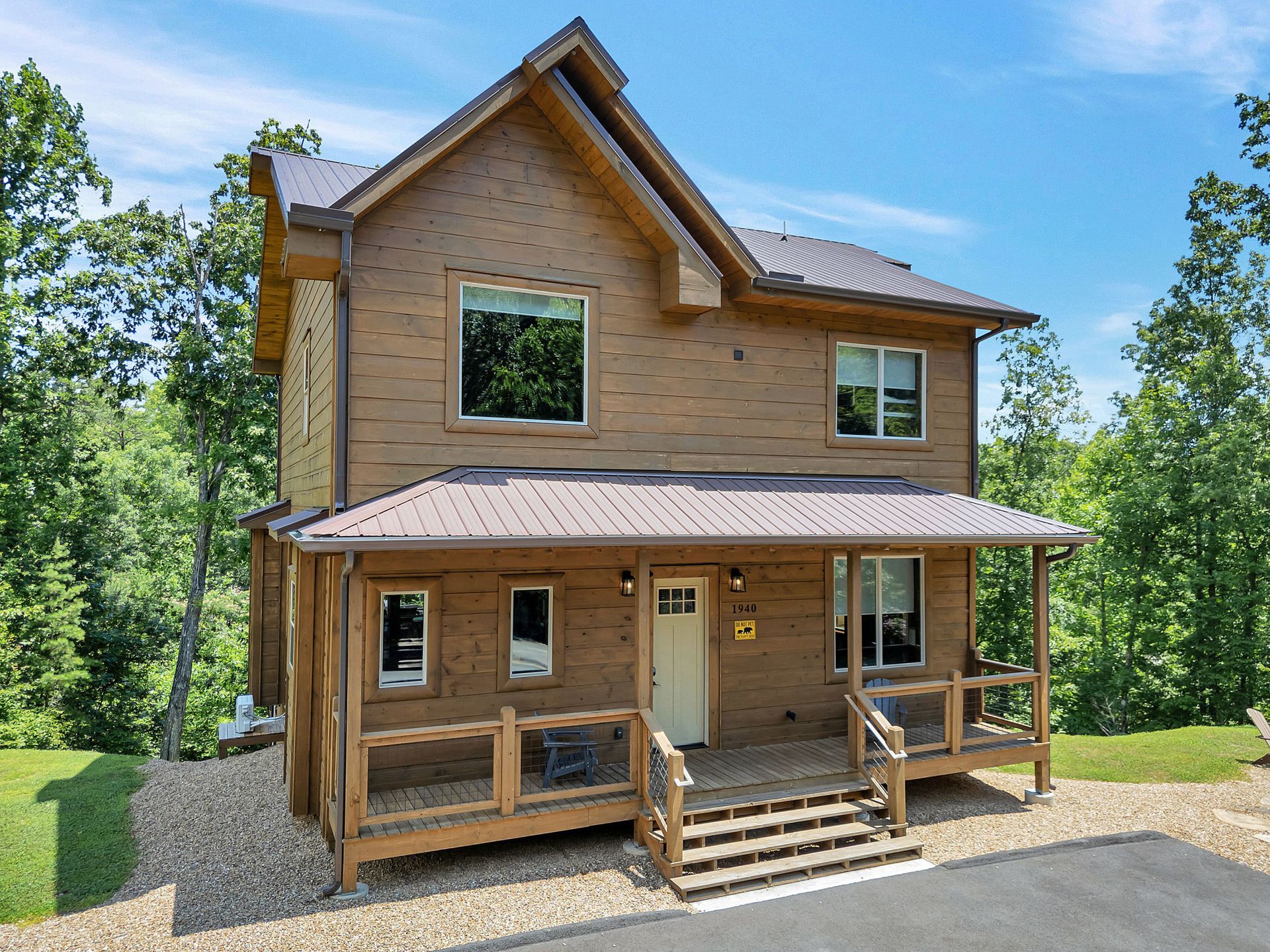 Brown cabin with covered porch, surrounded by trees, on a sunny day.