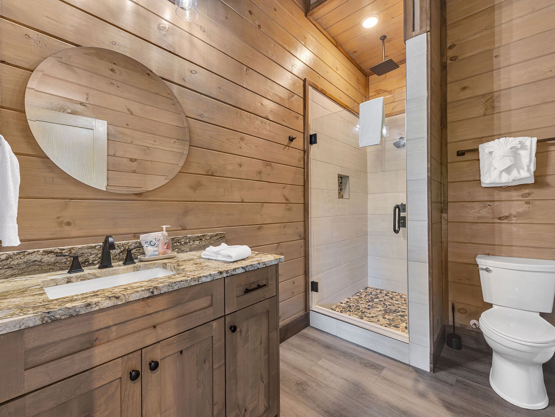 Bathroom with wooden walls, vanity, shower with pebble floor, and toilet.