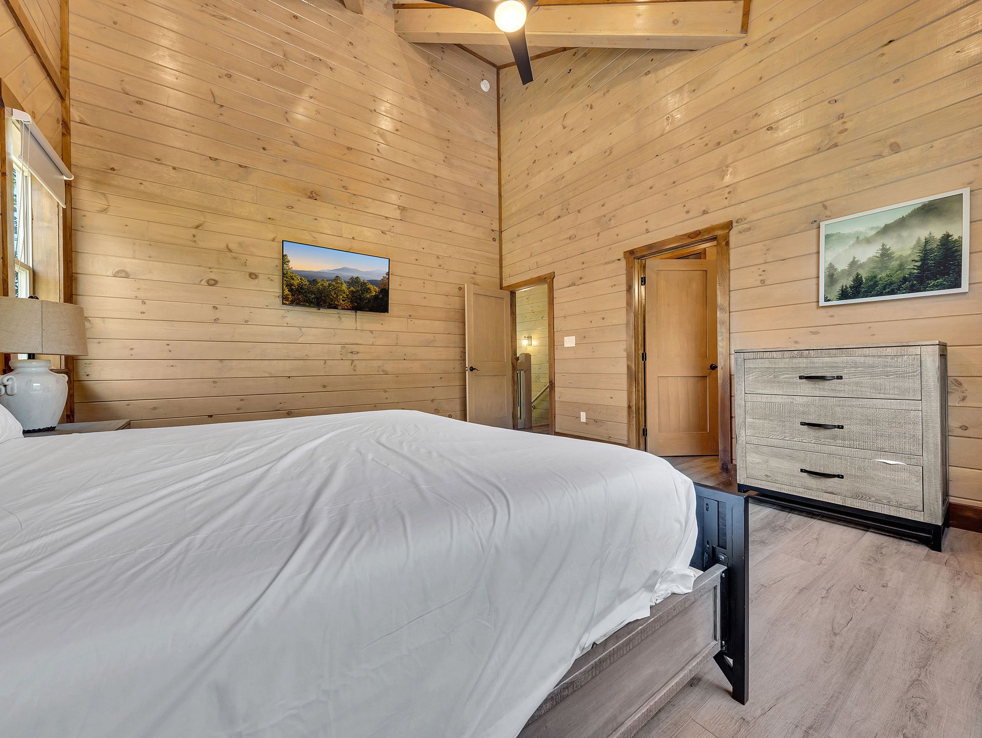 Bedroom with wood walls, a bed with white linens, and a dresser.