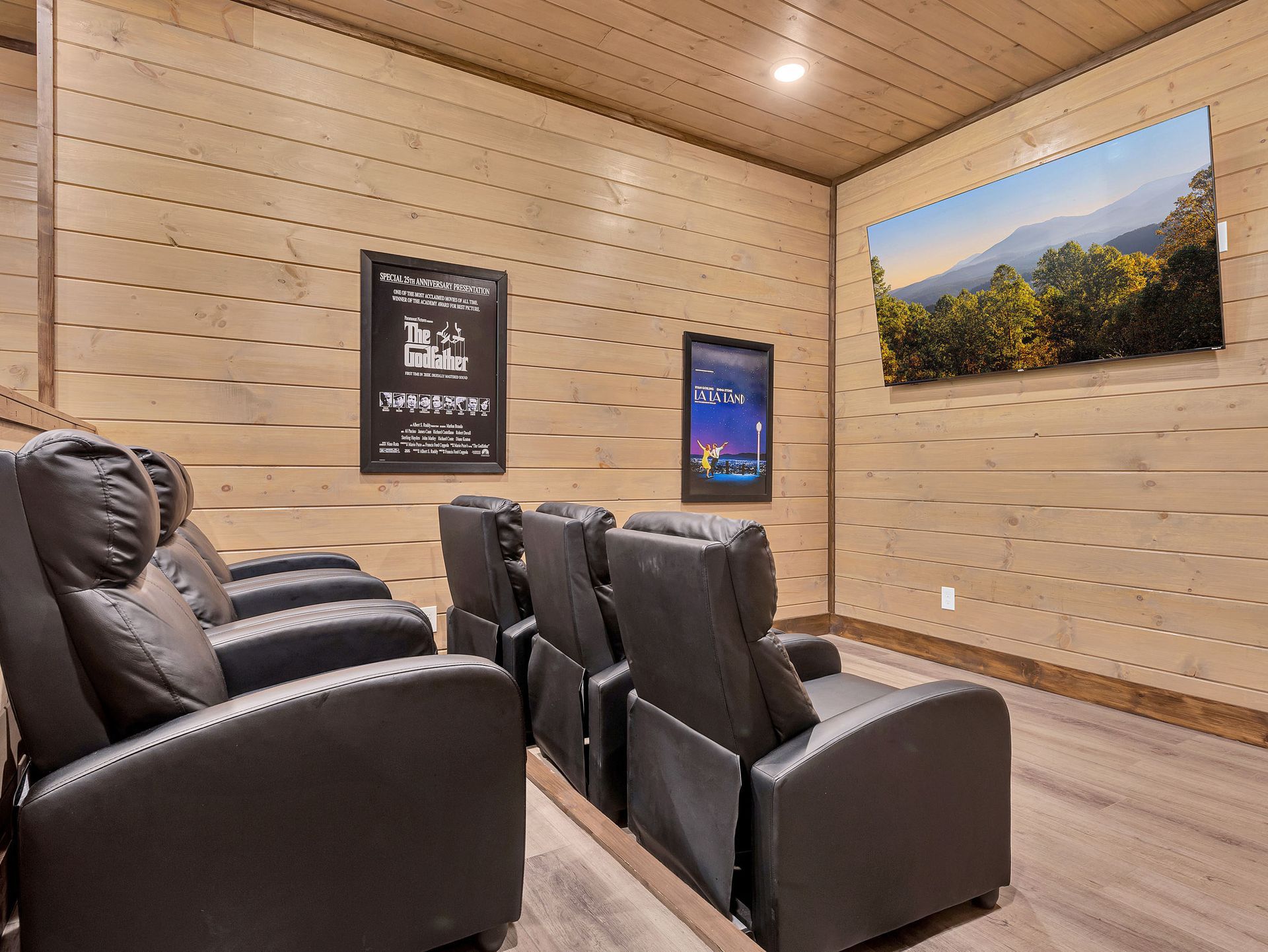 Home theater room with reclining black leather chairs, wooden paneling, and large screen displaying a landscape.