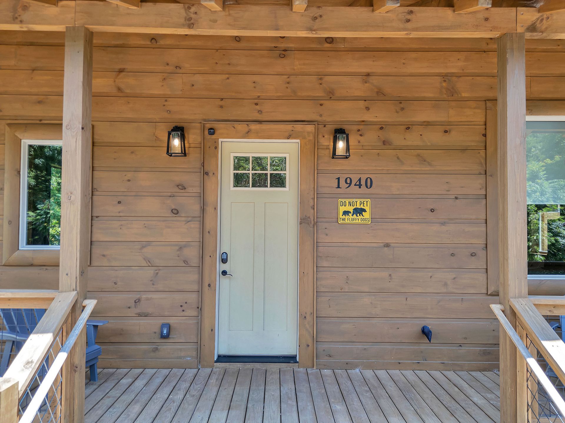 Wooden cabin entrance with porch. Beige door, address 1940, two black lights.
