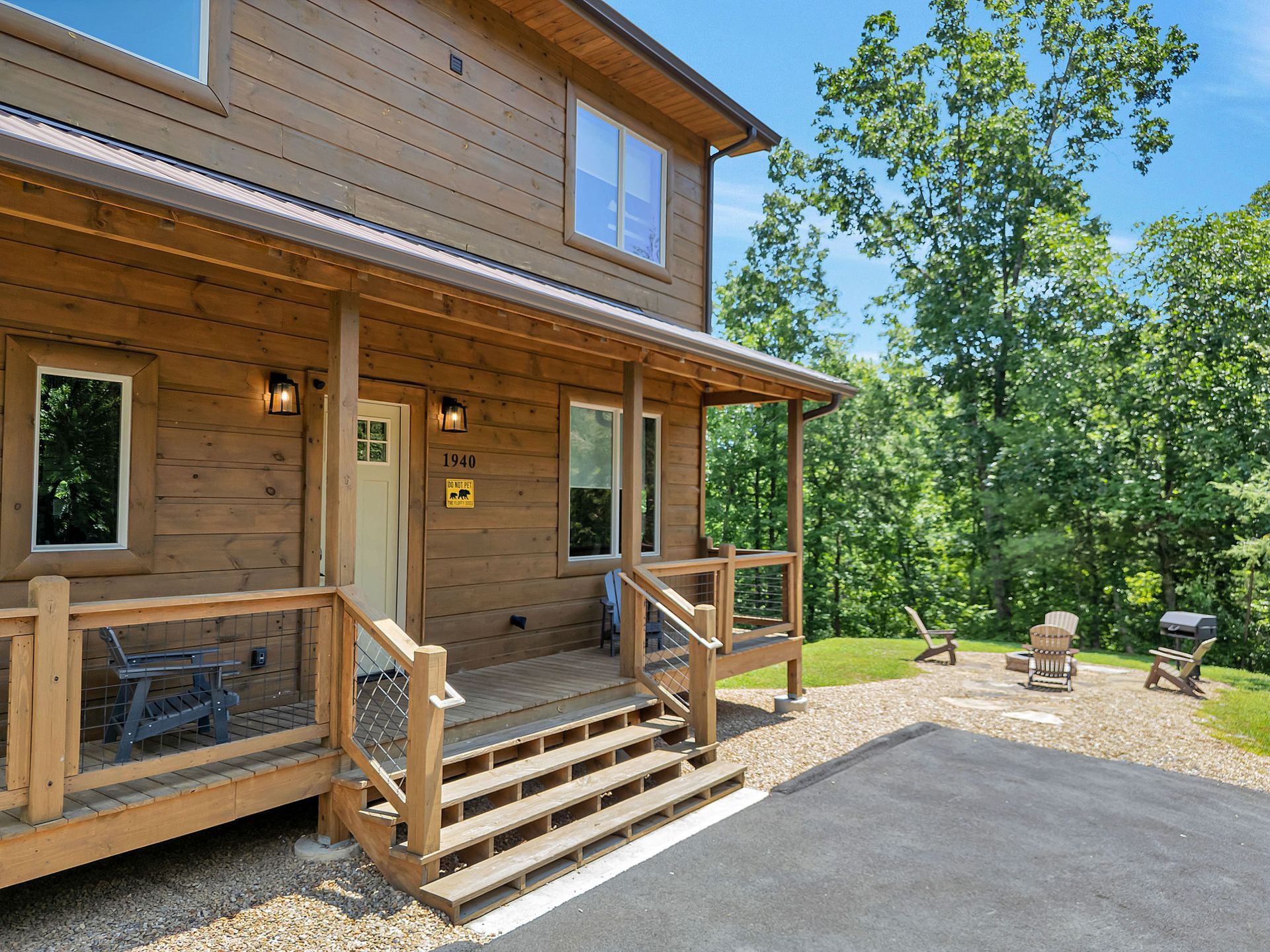 Rustic brown cabin with a porch and steps, surrounded by trees and a gravel yard.