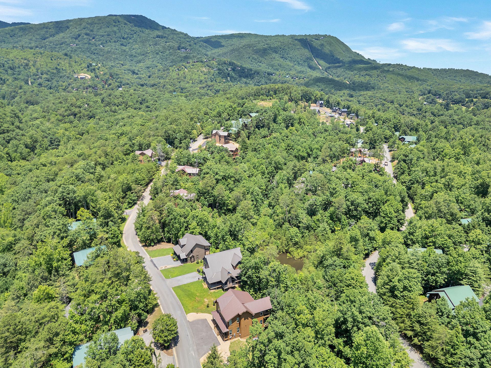 Aerial view of mountain cabins nestled in a lush, green forest, with roads winding through.
