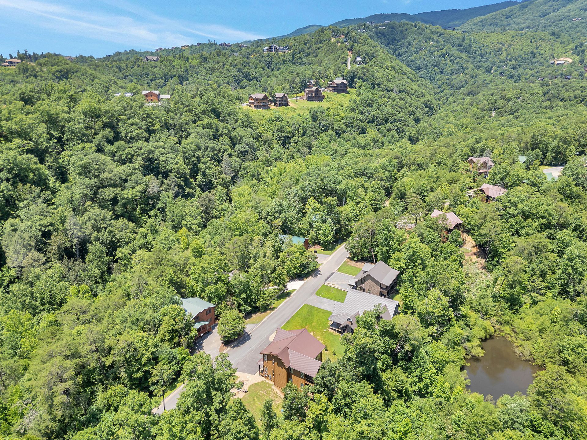 Aerial view of cabins nestled in lush, green mountain landscape with a pond.