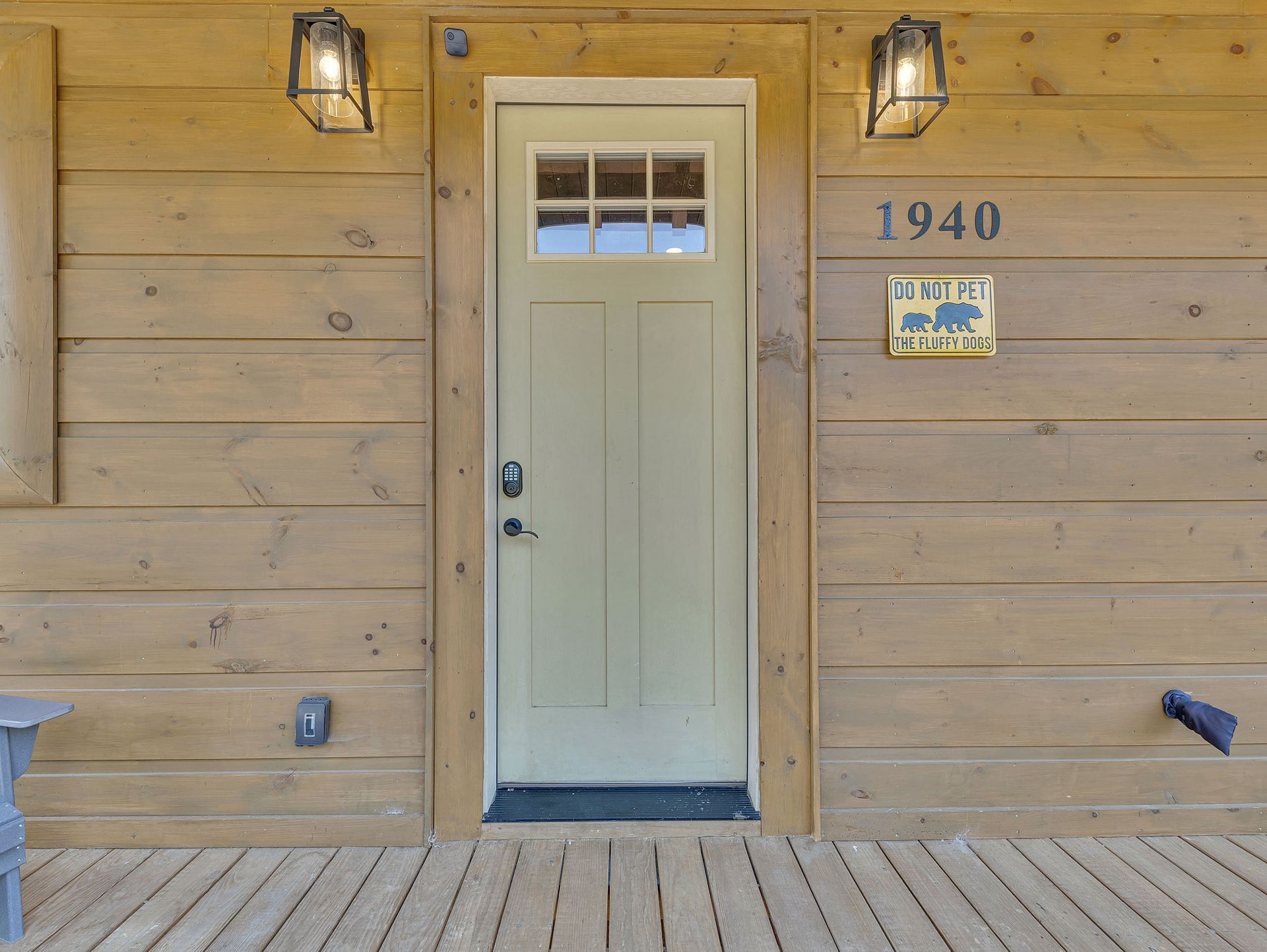 Wooden cabin entrance with a tan door, address 1940, and two lanterns.