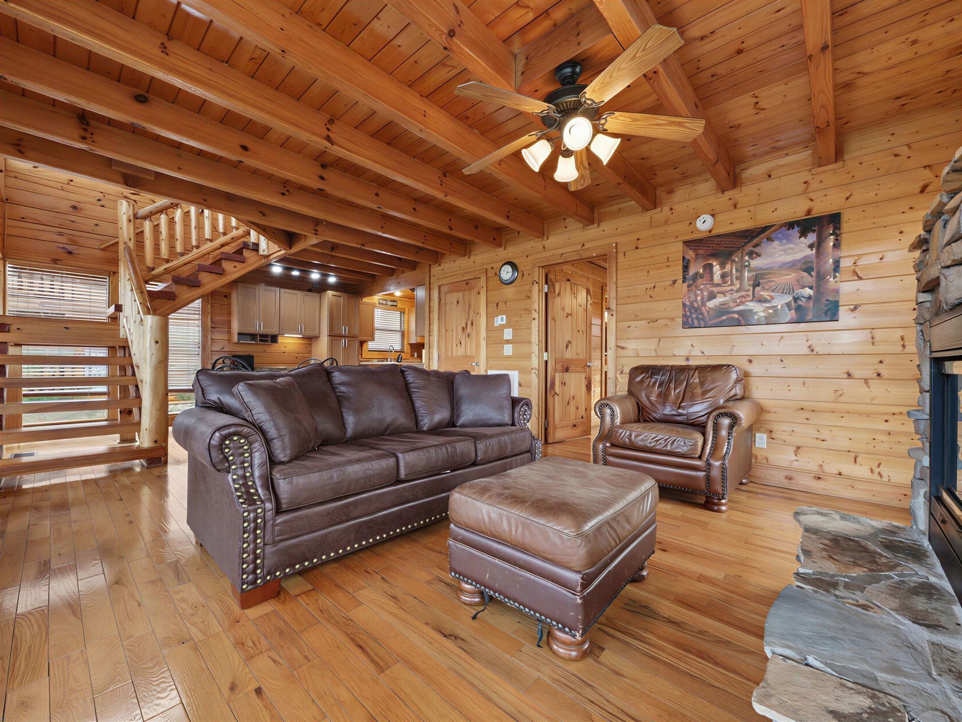 Cozy cabin living room with leather furniture, fireplace, and wooden beams.