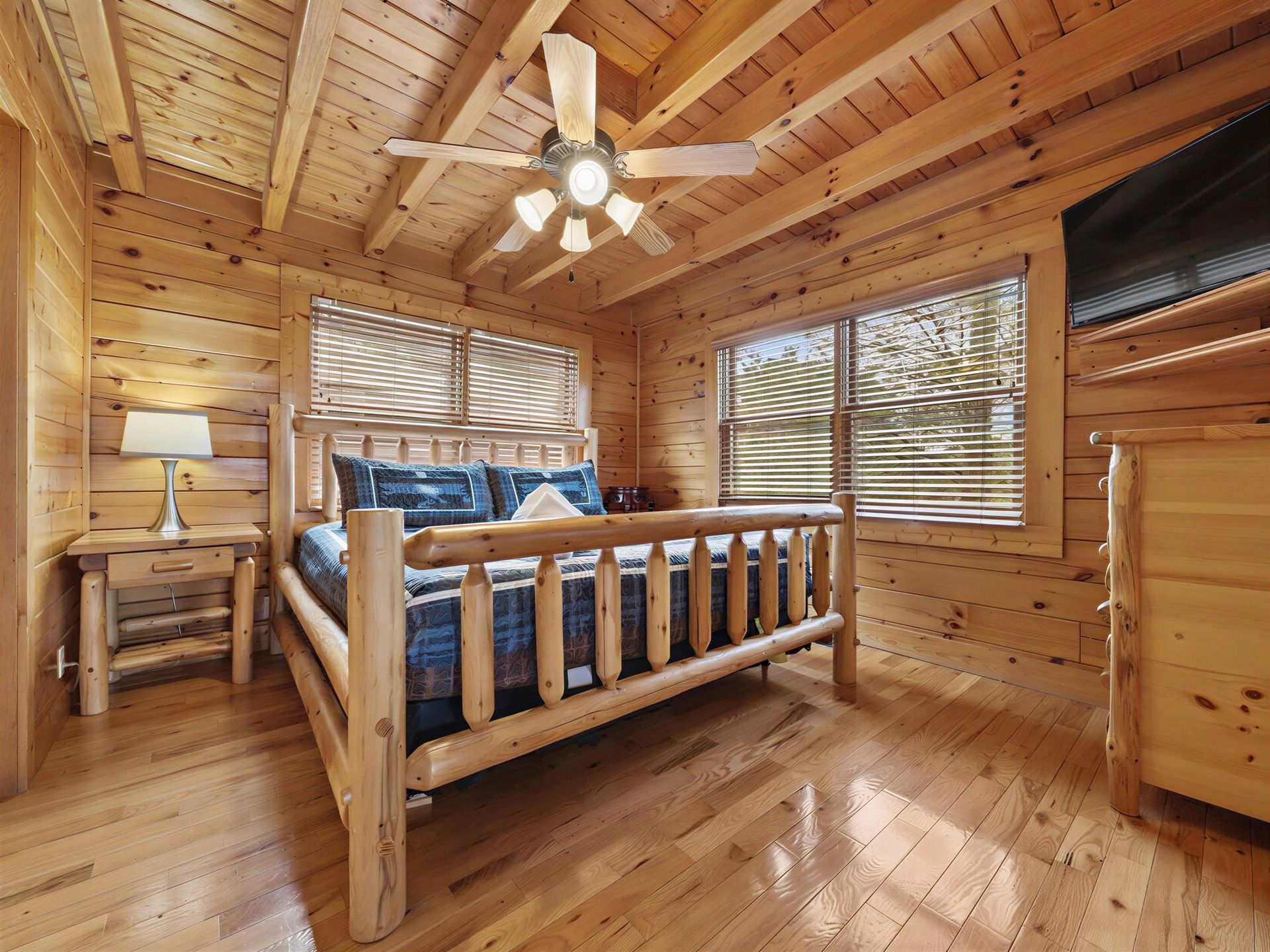 Wooden bedroom with a bed, windows, lamp, and ceiling fan.