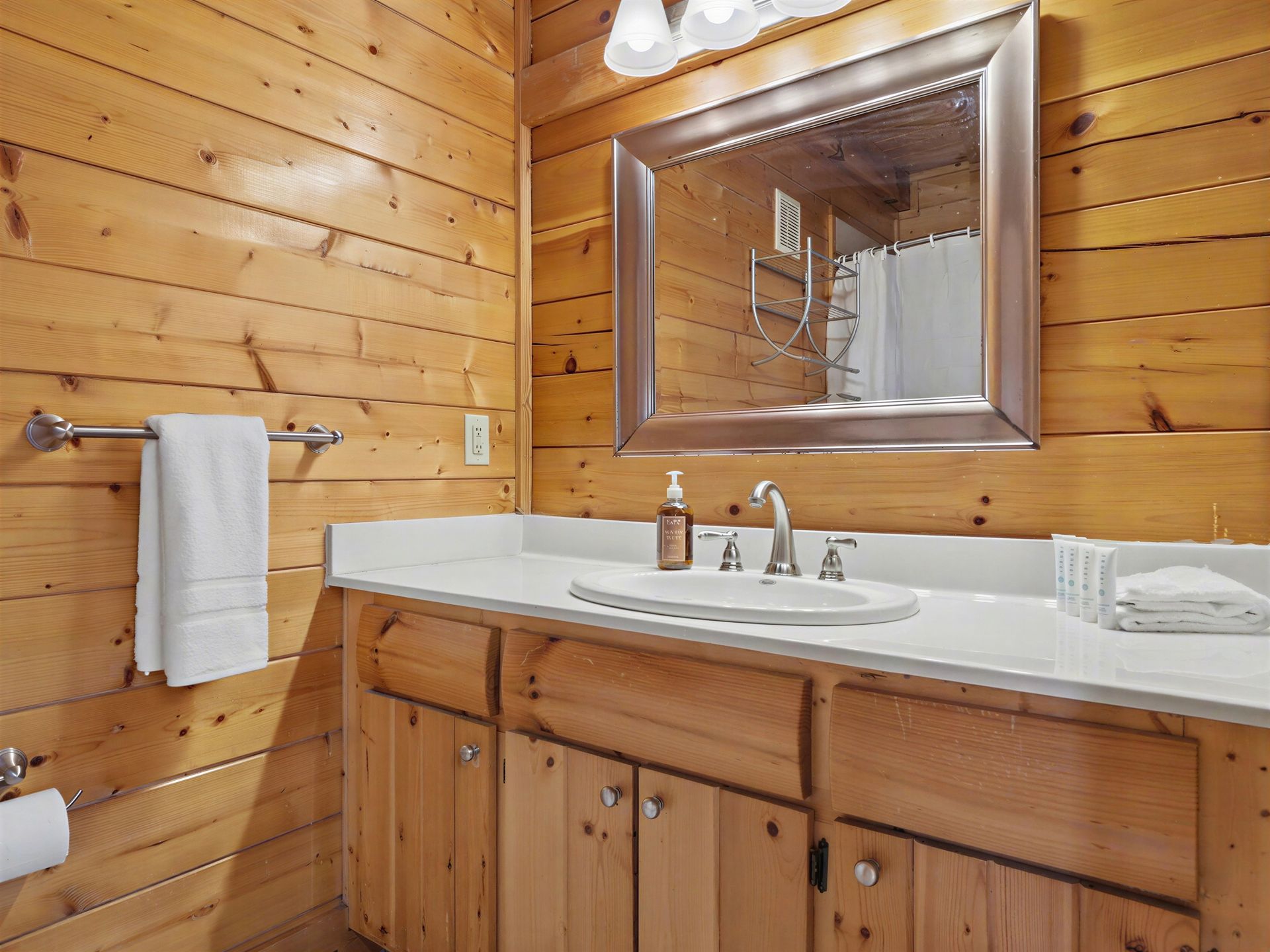 Bathroom with wood paneled walls, white countertop, and light wood cabinets.