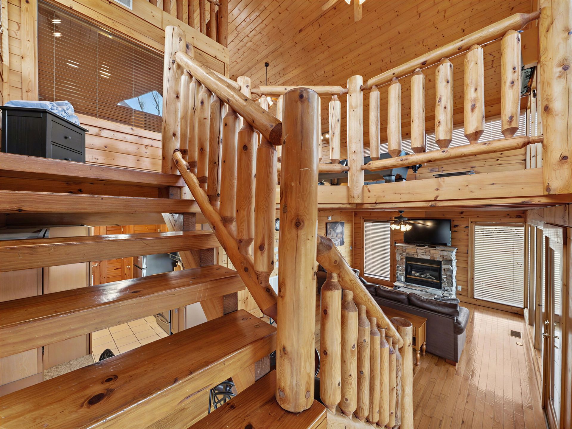 Wooden log staircase in a cabin. Balcony overlooks a living room with fireplace and furniture.