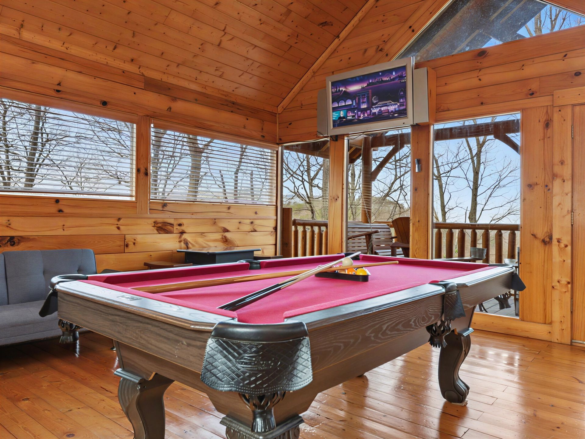 Pool table in a wood-paneled room with a TV and windows overlooking trees.