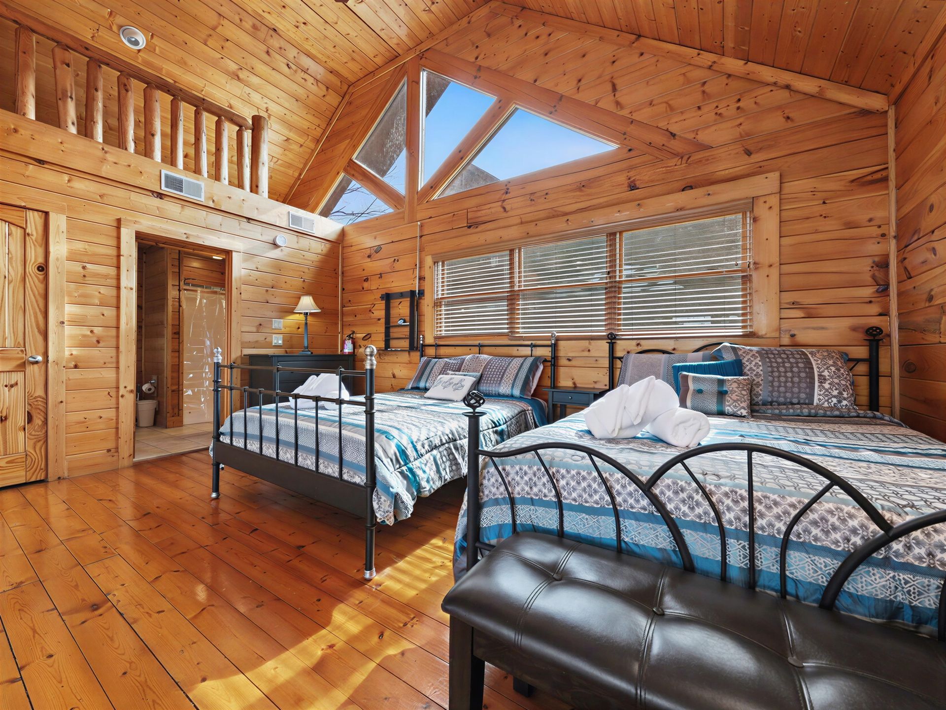 Bedroom in a cabin with wood walls, two beds, a loft, and natural light from triangular windows.