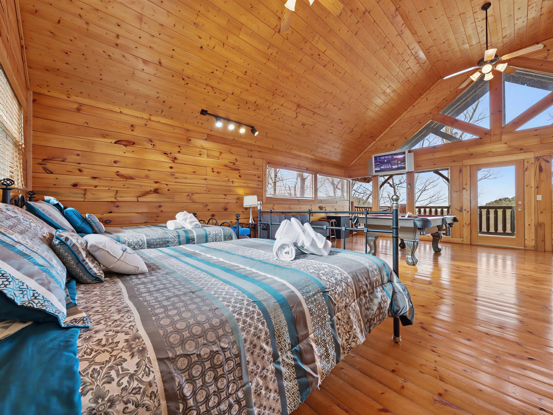 Bedroom with two beds, wooden walls/ceiling, windows, foosball table, and mountain view.