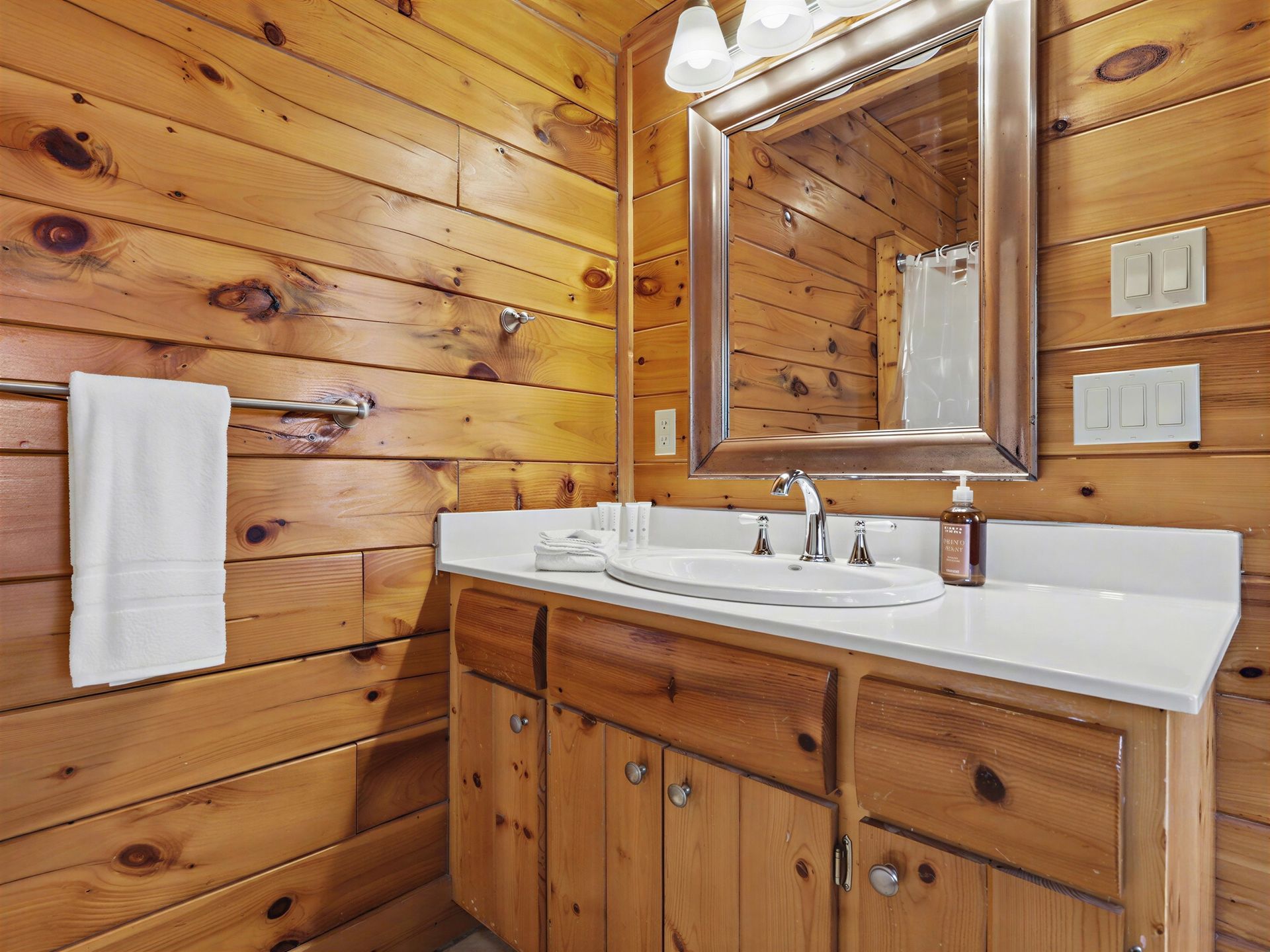 Bathroom with wooden walls and cabinets, white countertop and sink, mirror, towel bar, and white towel.