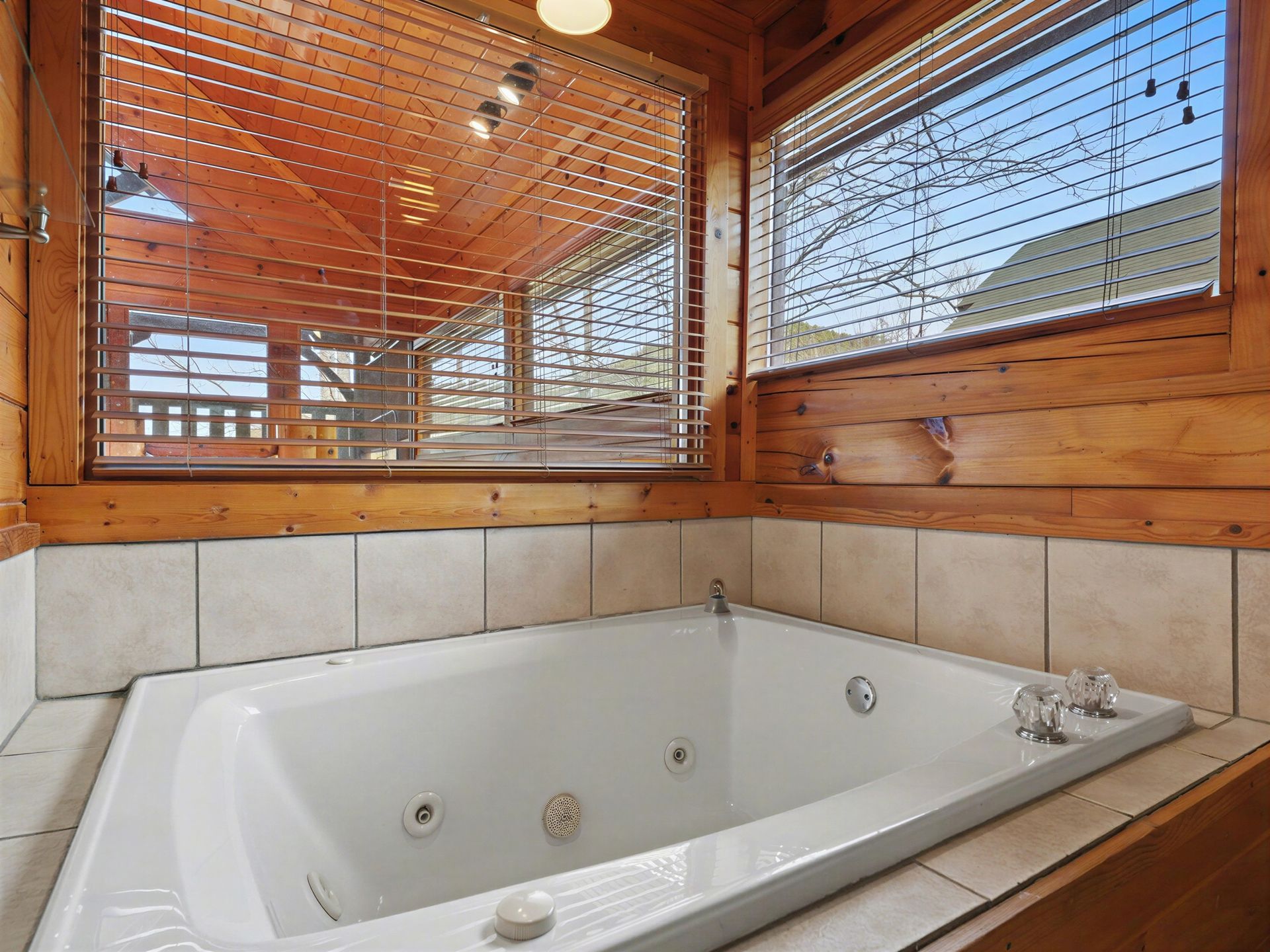 Jacuzzi tub in a wood-paneled bathroom with views of a porch through blinds and a window.
