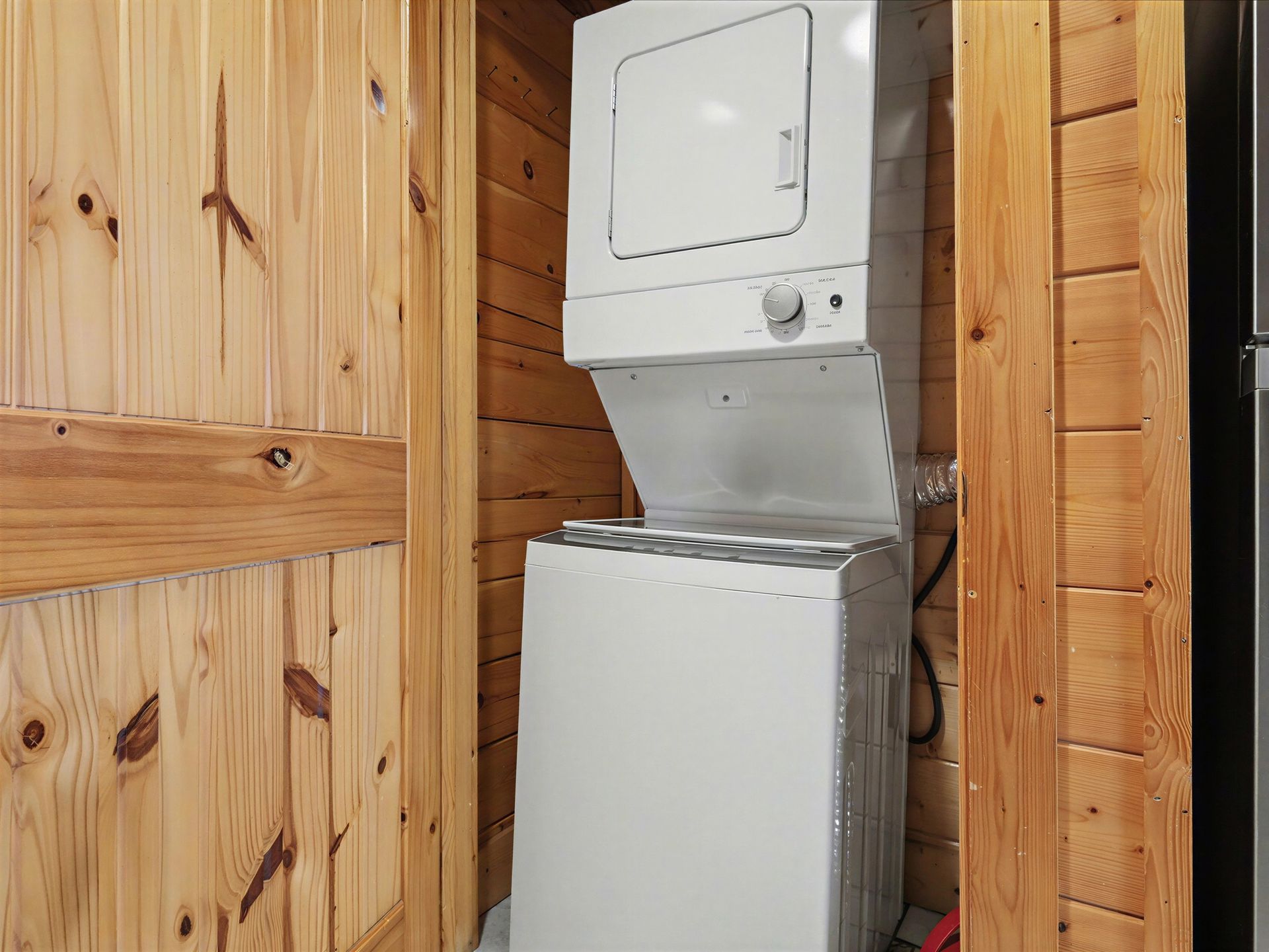 Stacked washer and dryer in a wooden-paneled room.