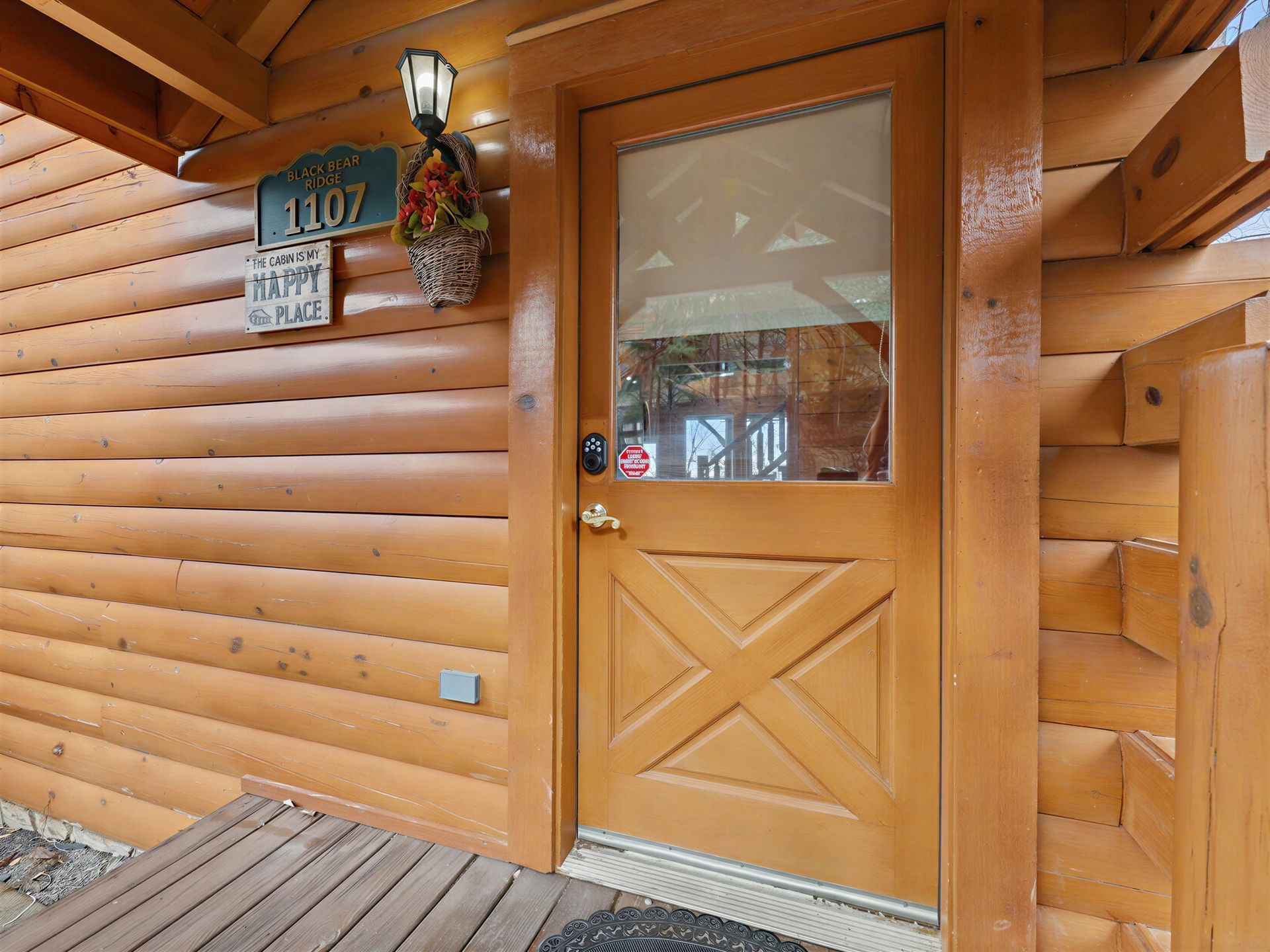 Wooden cabin entrance with a glass-paned door, a hanging basket, and address signs.