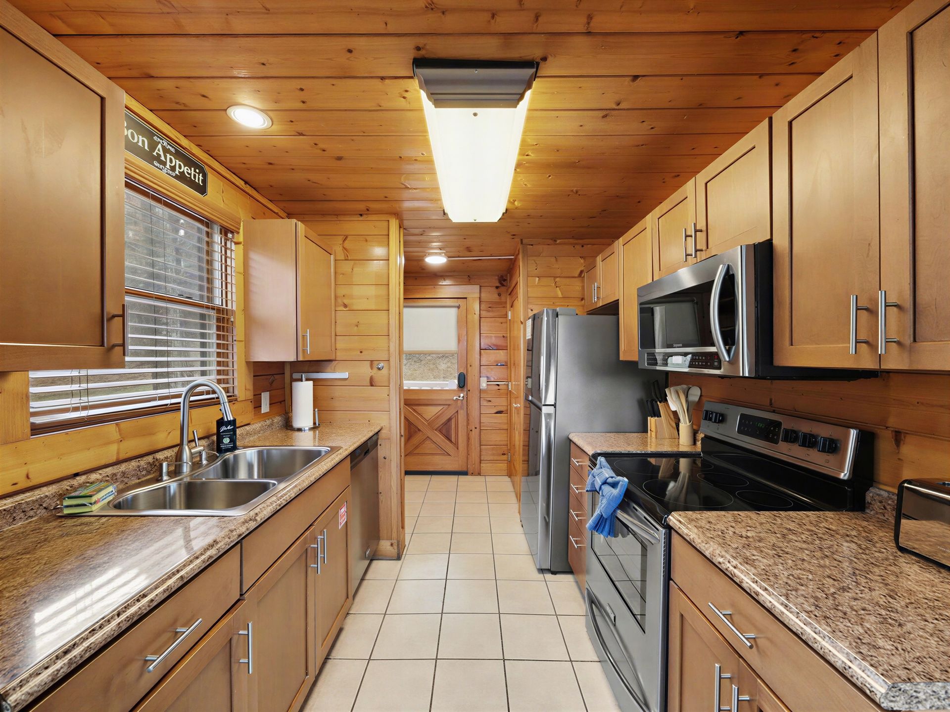 Wooden-cabin kitchen with light-brown cabinets, stainless-steel appliances, and a window.