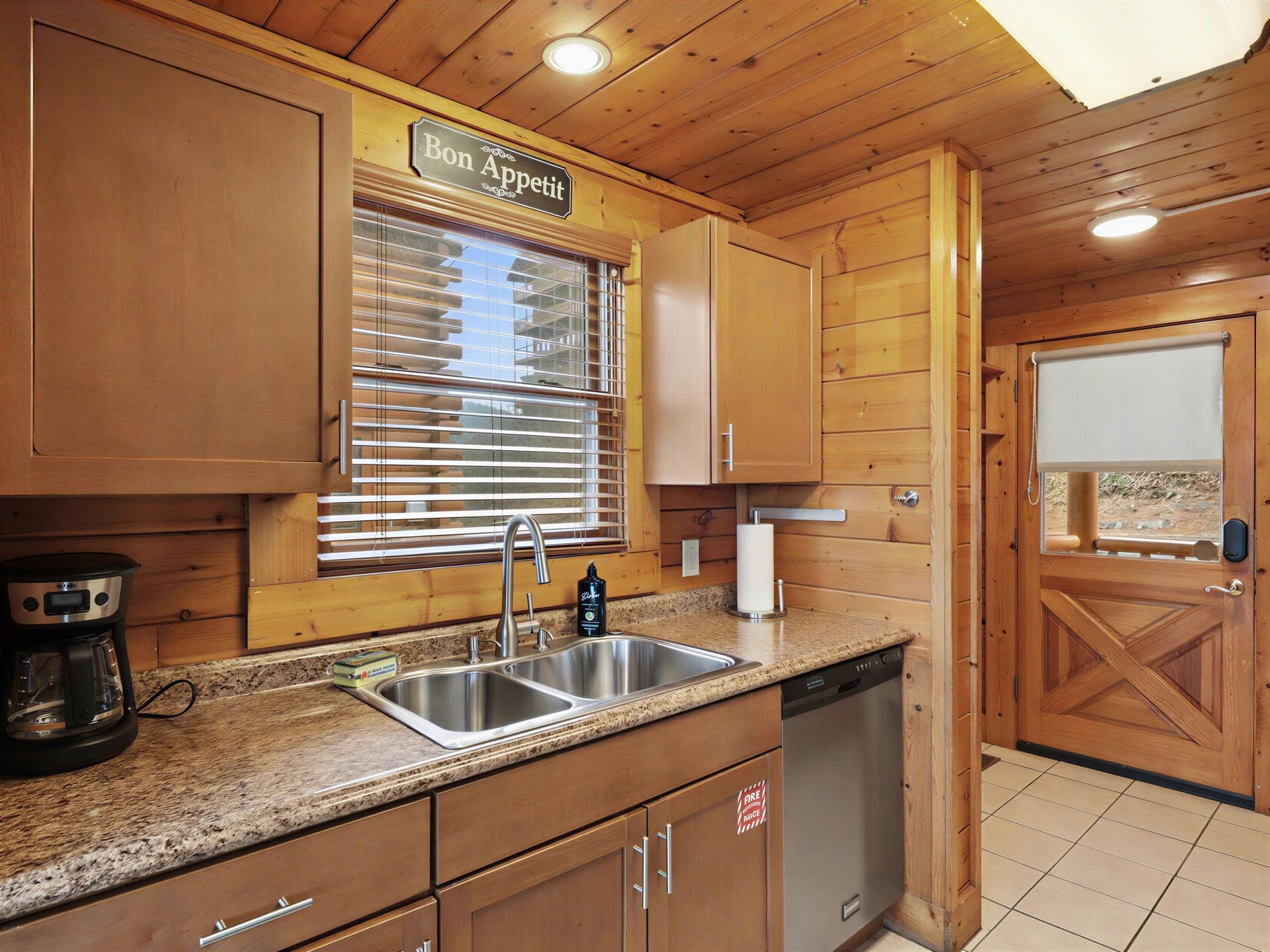 Wooden cabin kitchen with cabinets, sink, window, and a door.