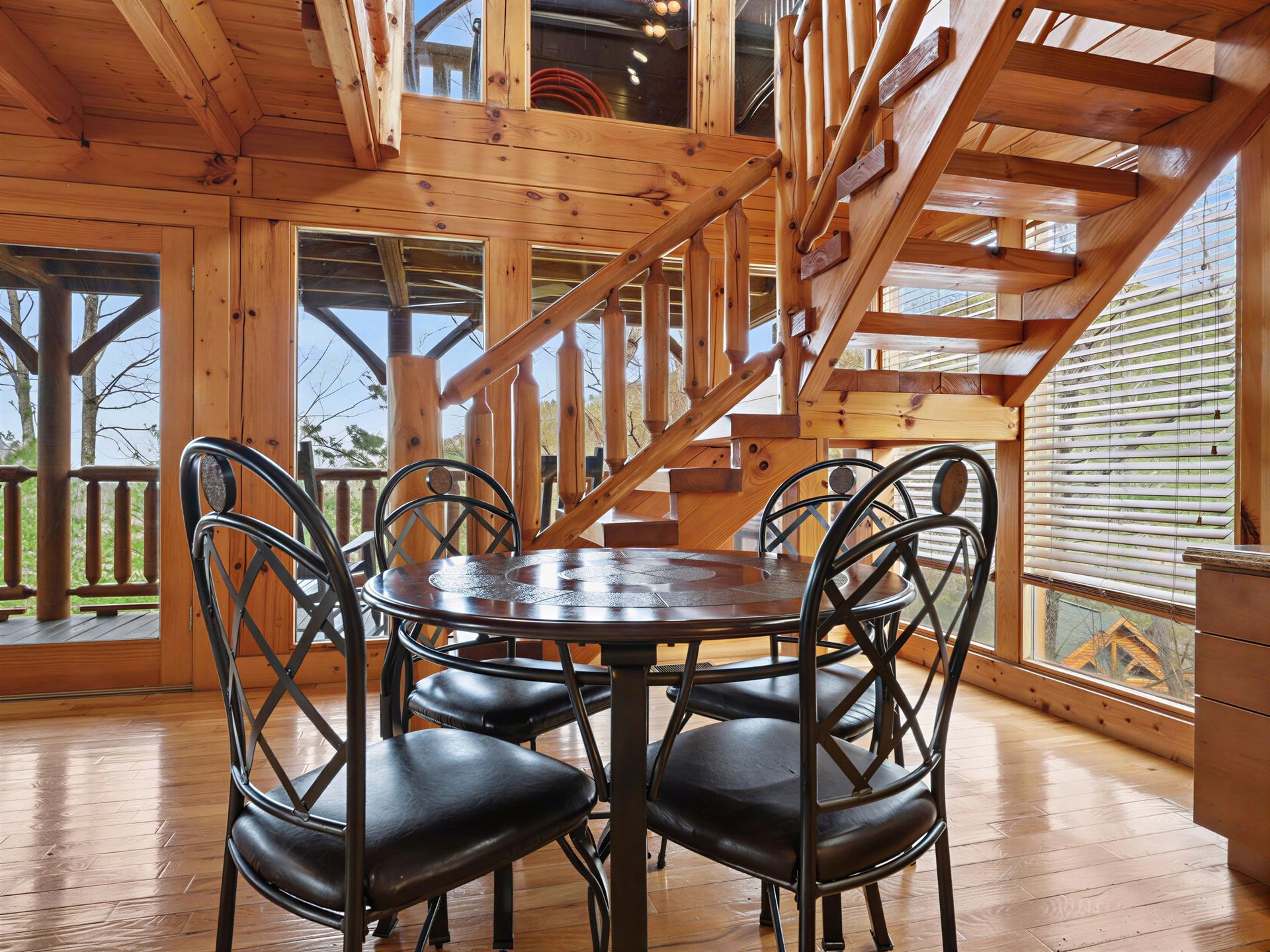 Dining room with round table and four black chairs, wooden staircase in background.