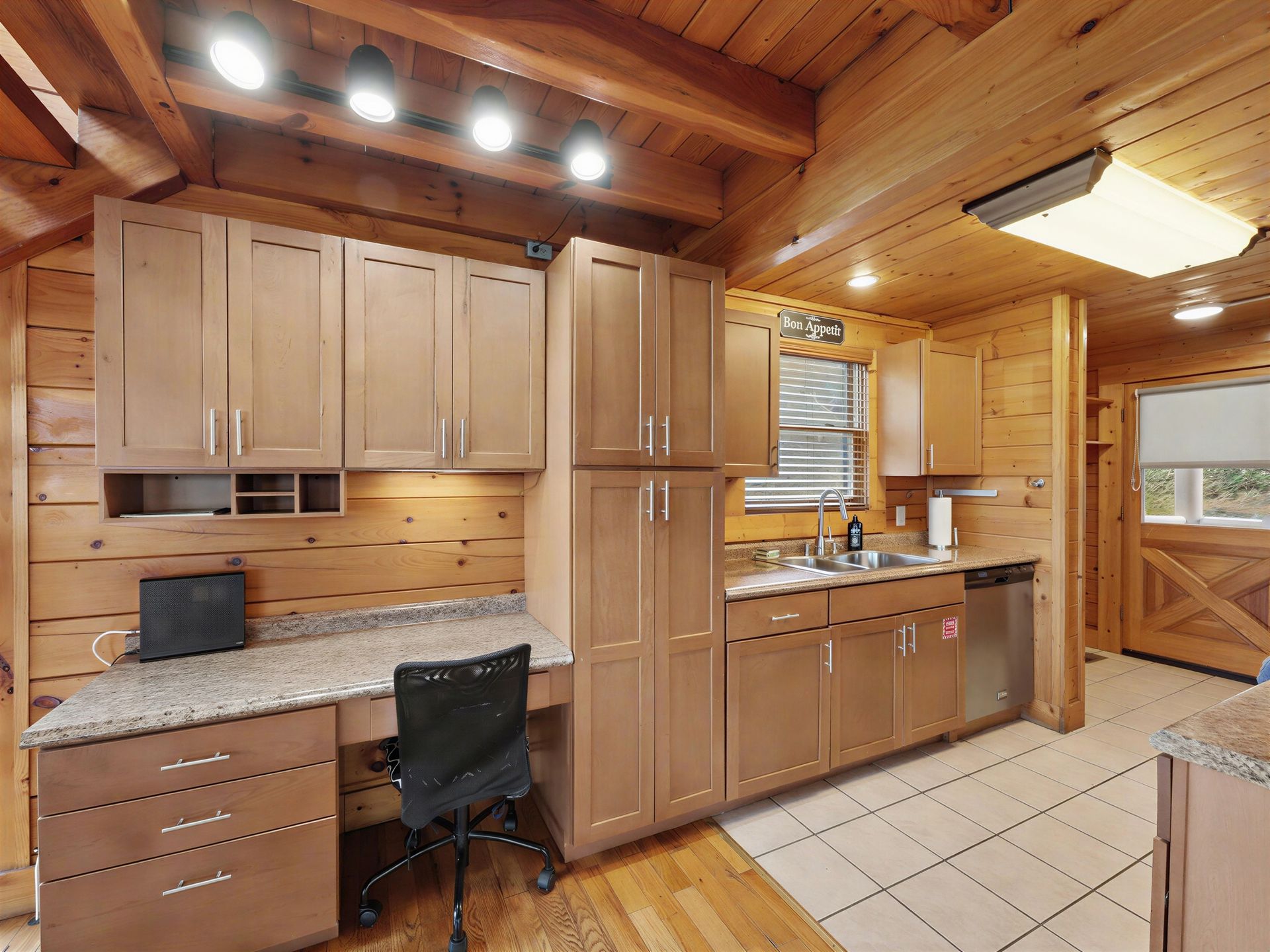 Kitchen with wooden cabinets and desk area, next to a window. Light wood paneling throughout.