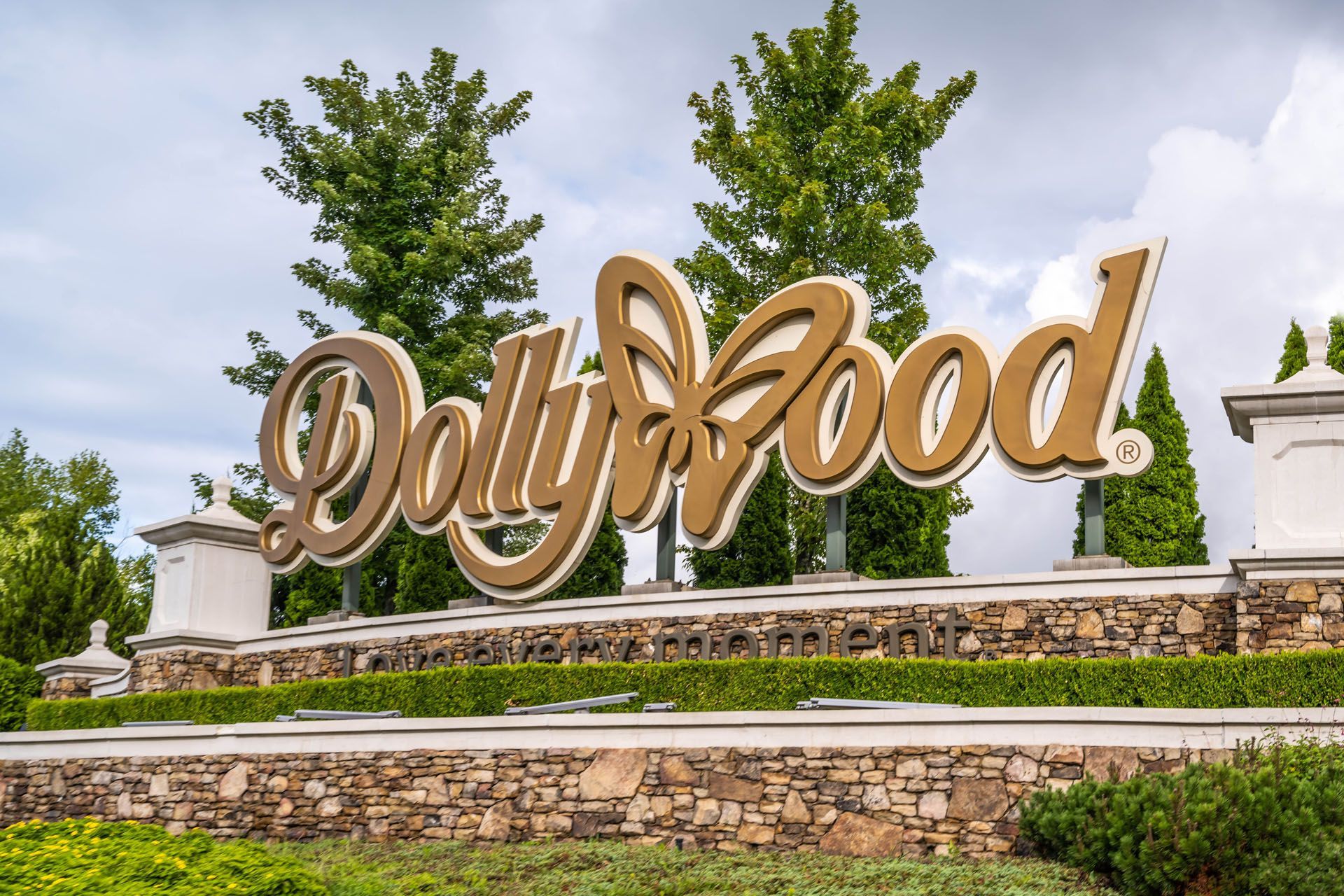 Sign for Dollywood amusement park, gold lettering with a butterfly on a stone wall.