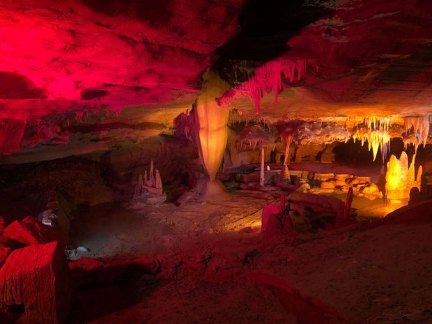 Cave interior illuminated with red and yellow lights, showcasing stalactites and stalagmites.