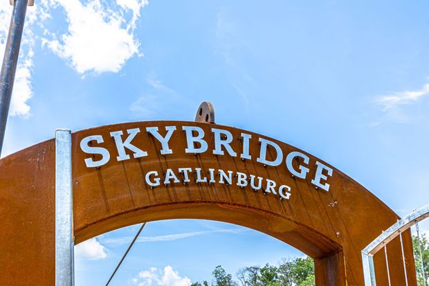 Skybridge Gatlinburg sign, brown arched entrance with white letters, against a blue sky with clouds.