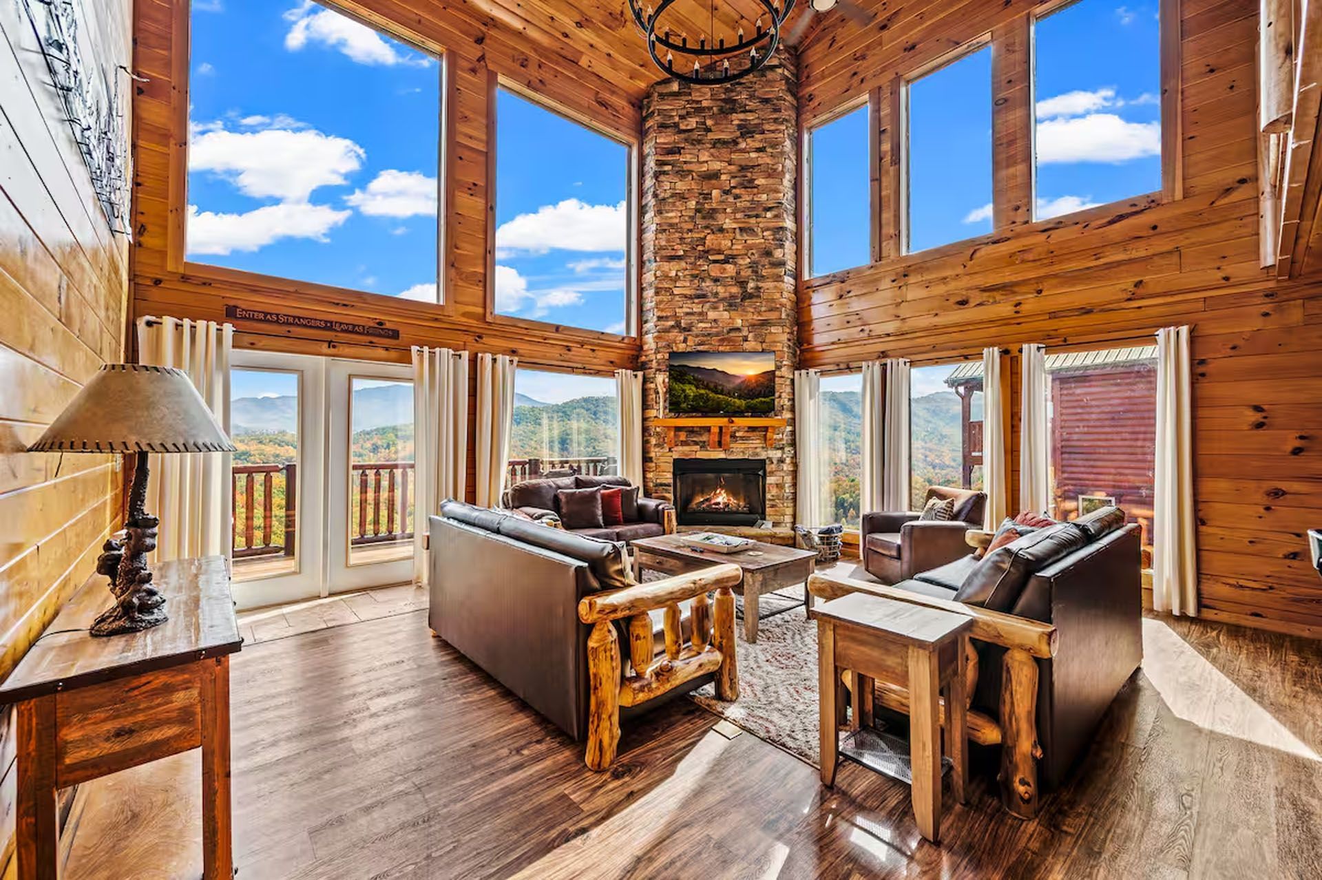 Lodge living room with high windows, stone fireplace, and wood furniture overlooking a mountain view.
