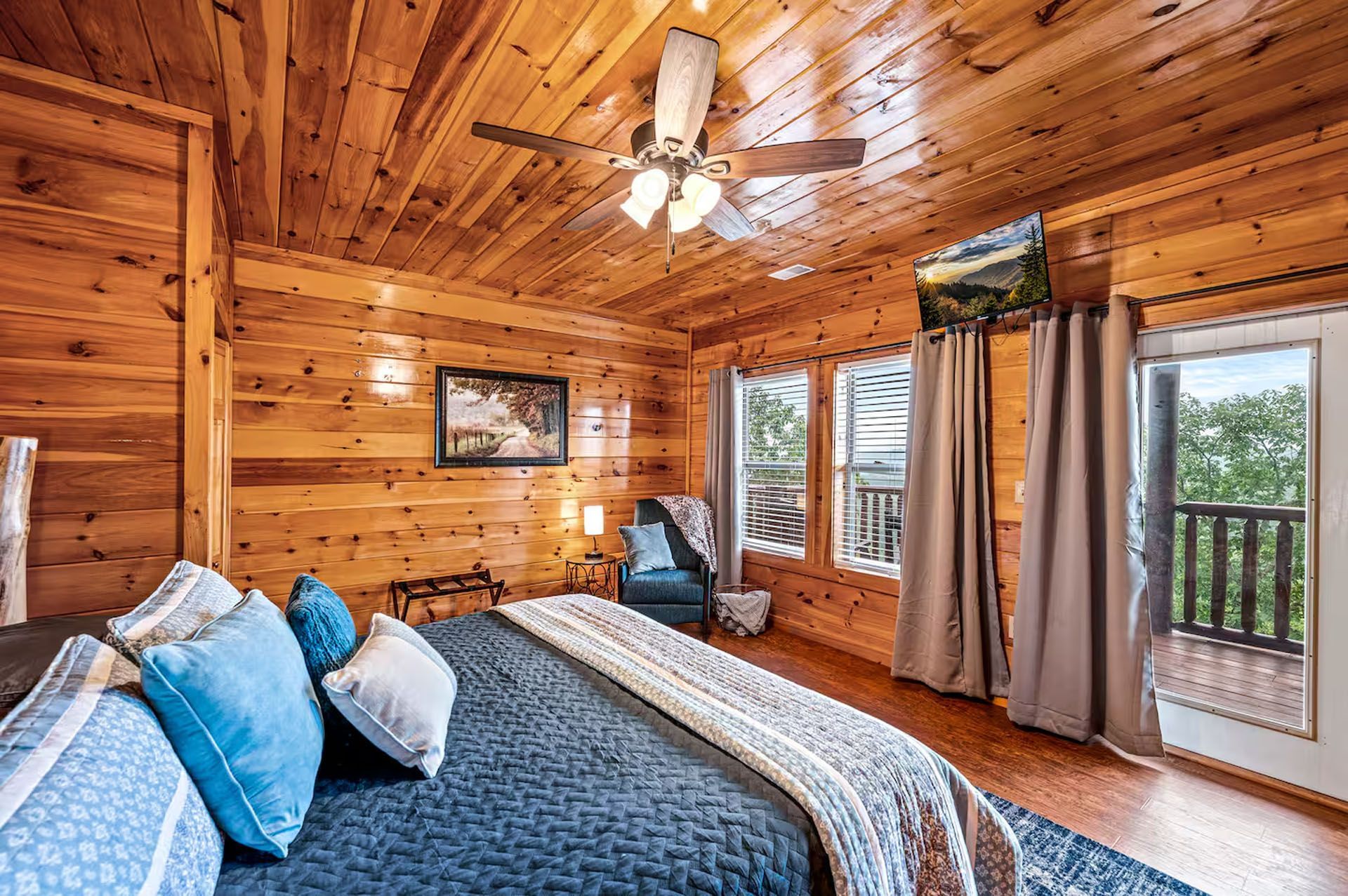 Wooden bedroom with a bed, TV, and balcony access. Blue and white bedding with light wood walls.