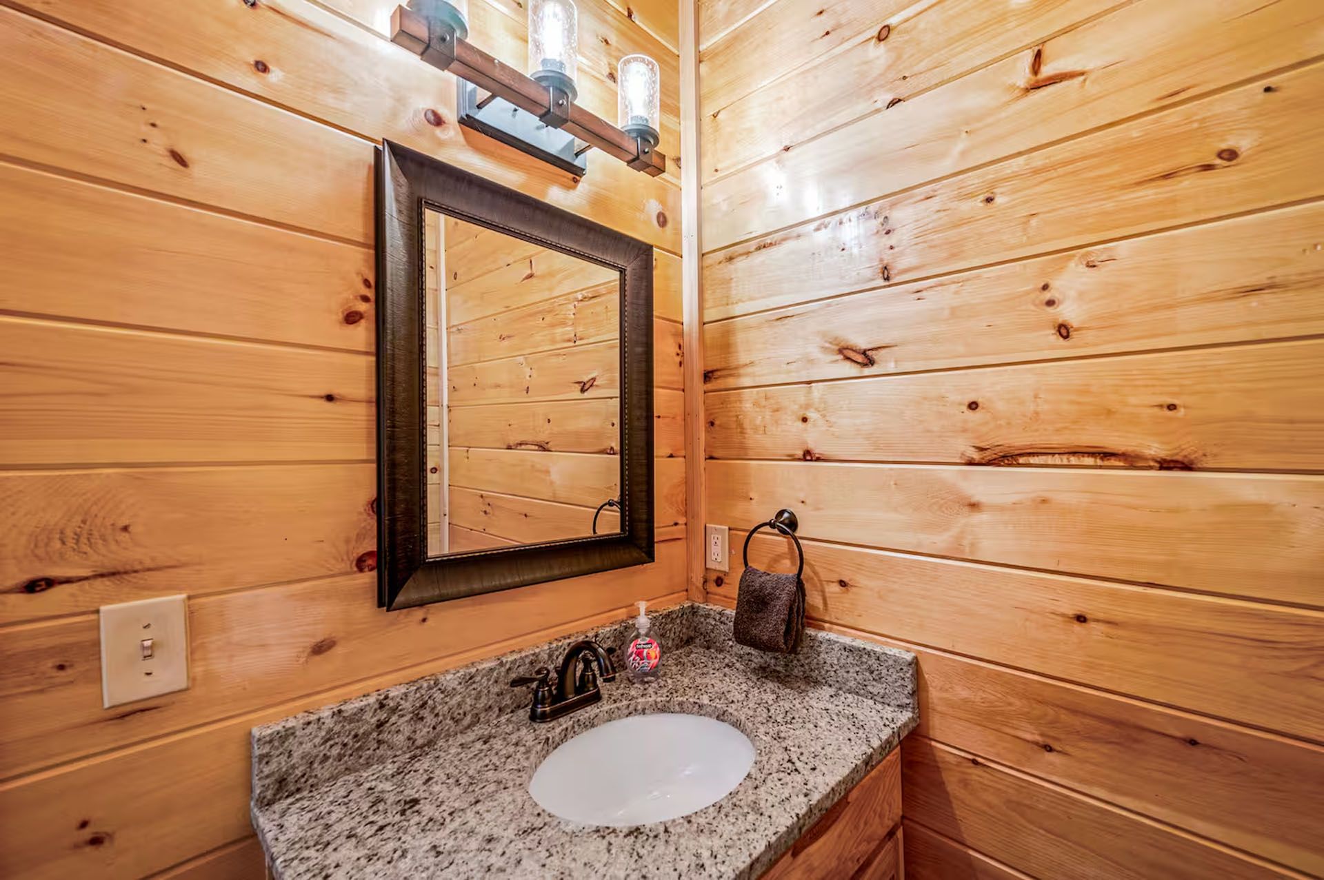Bathroom with light wood paneling, granite countertop, mirror, and sink.