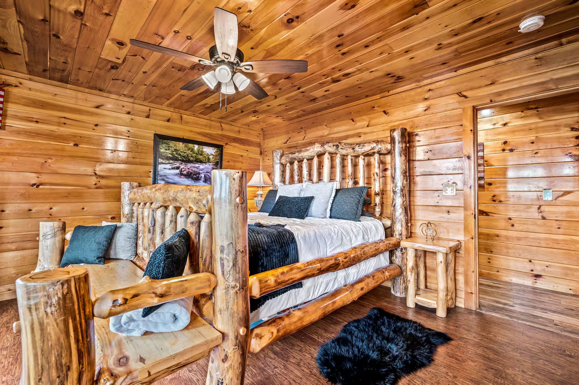 Rustic log cabin bedroom with wooden bed, ceiling fan, and dark rug.
