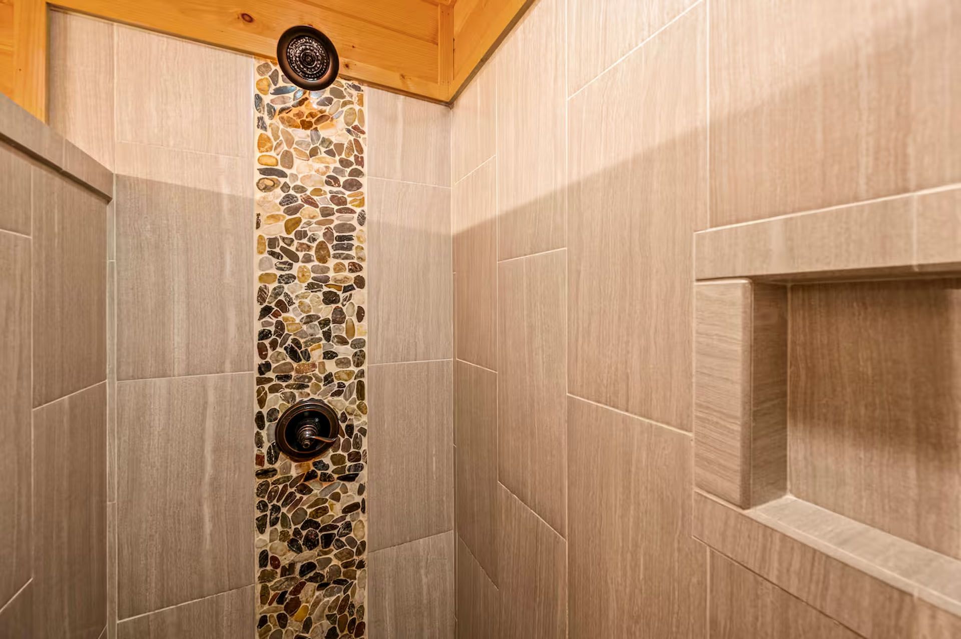 Shower stall with neutral-toned tile, a mosaic accent strip, and built-in shelf.