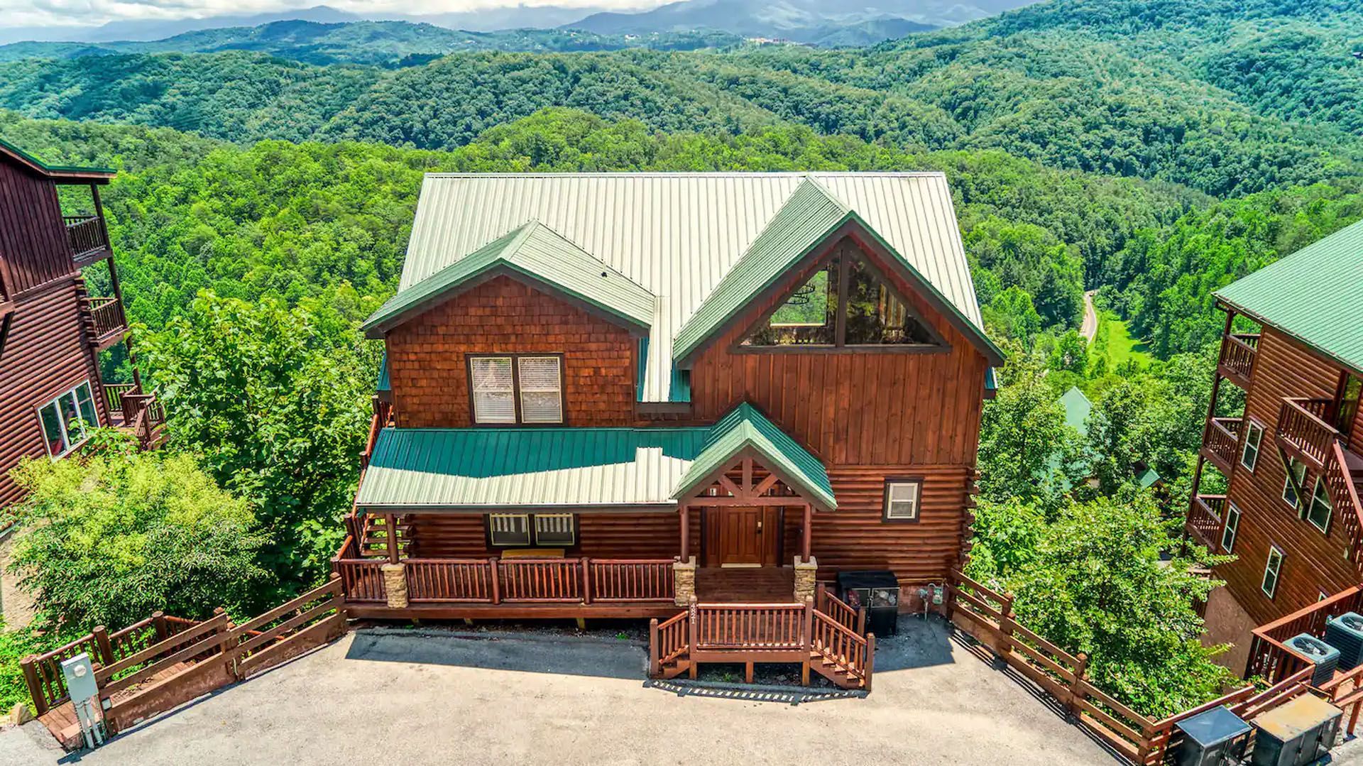Cabin nestled in lush green mountain landscape; brown wood with green roof accents.