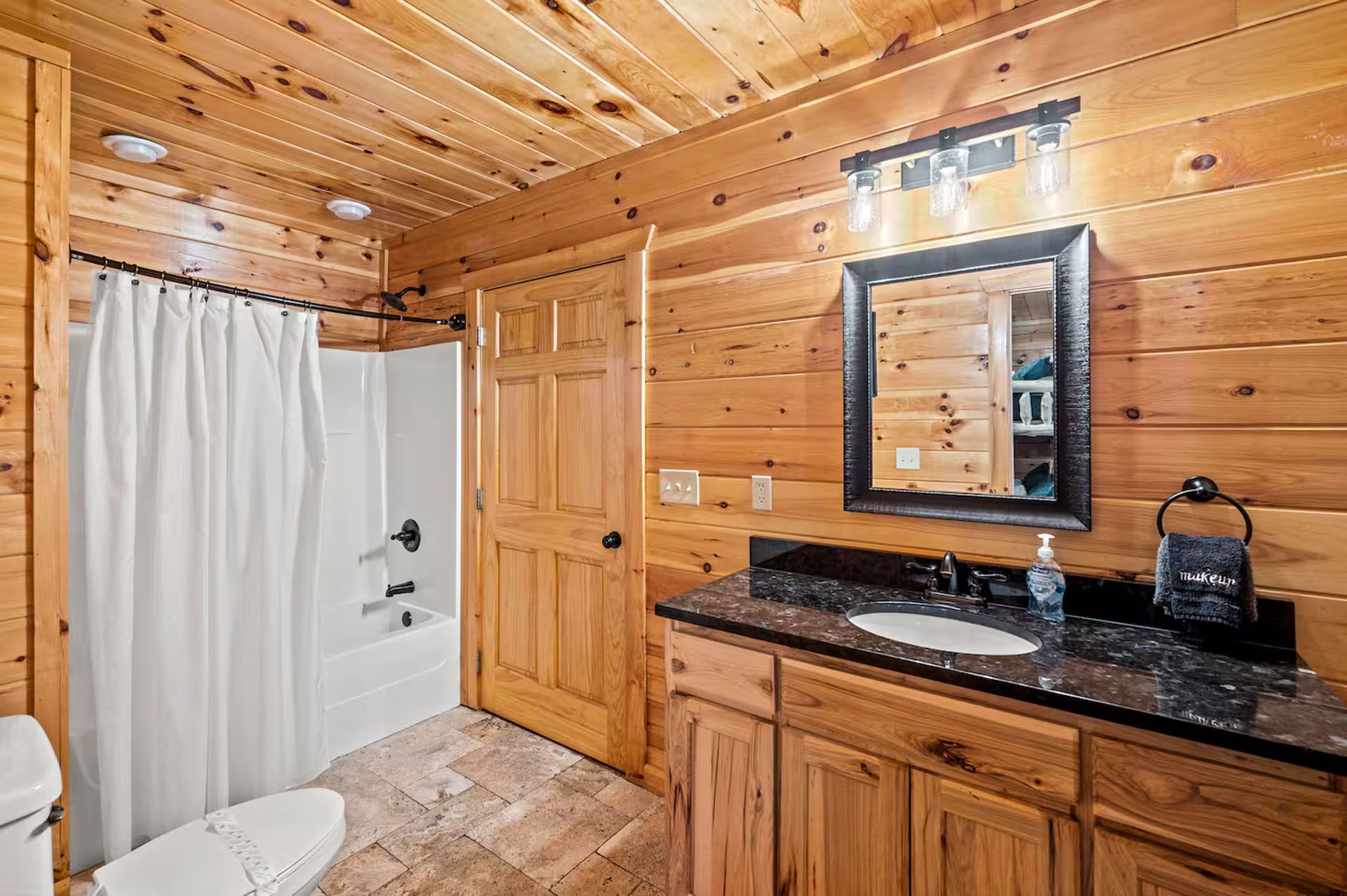 Bathroom with wood walls, sink, toilet, shower, and a vanity with a dark countertop.