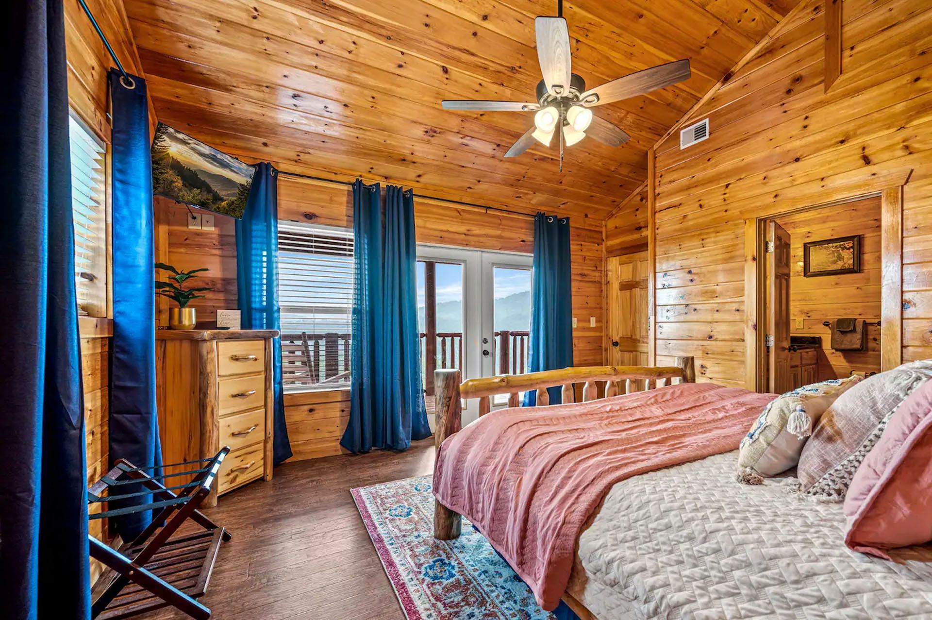 Wooden bedroom with bed, dresser, blue curtains, and door to balcony.