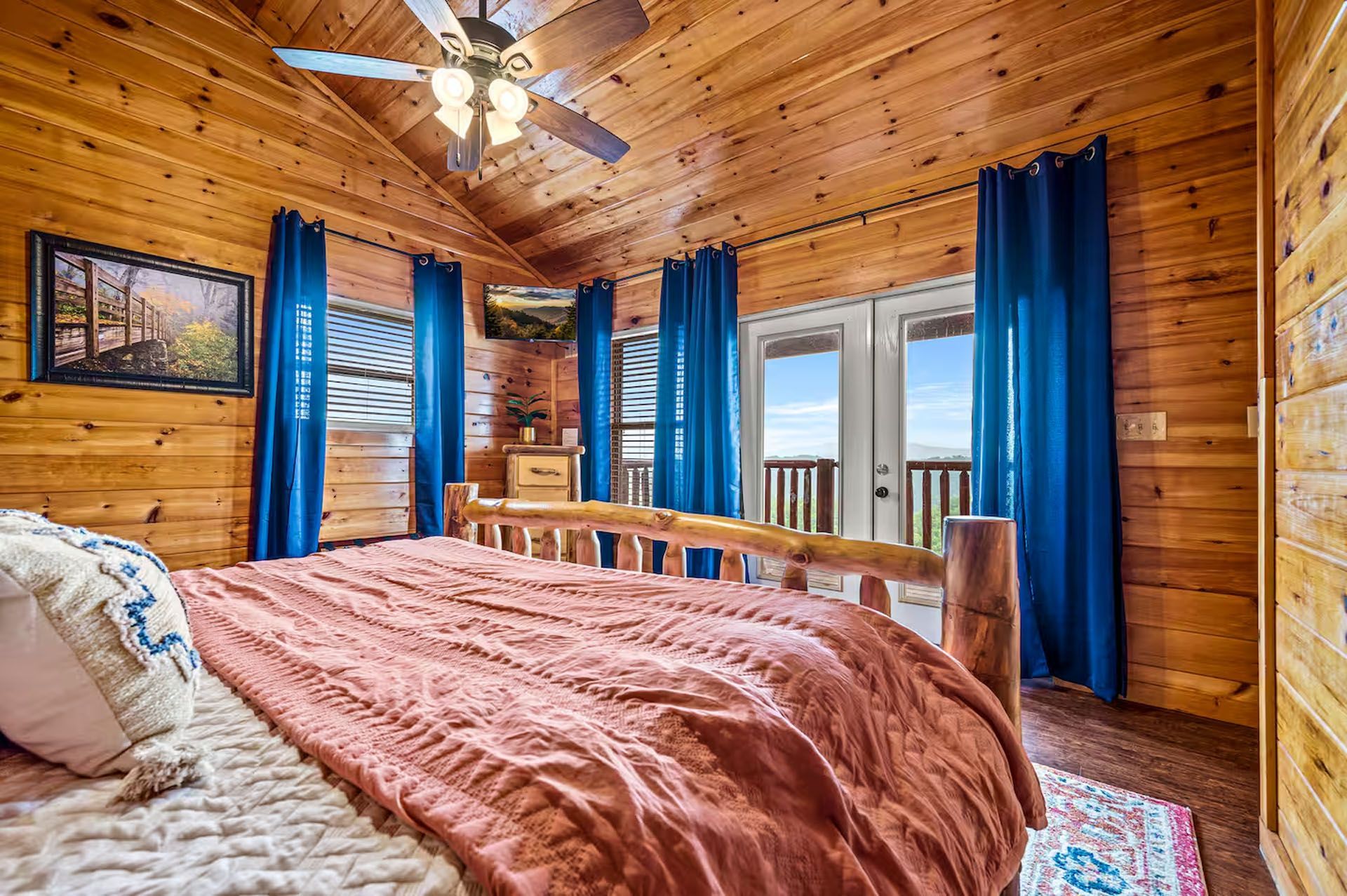 Bedroom with wooden walls, a large bed, and French doors leading to a balcony with a scenic view.