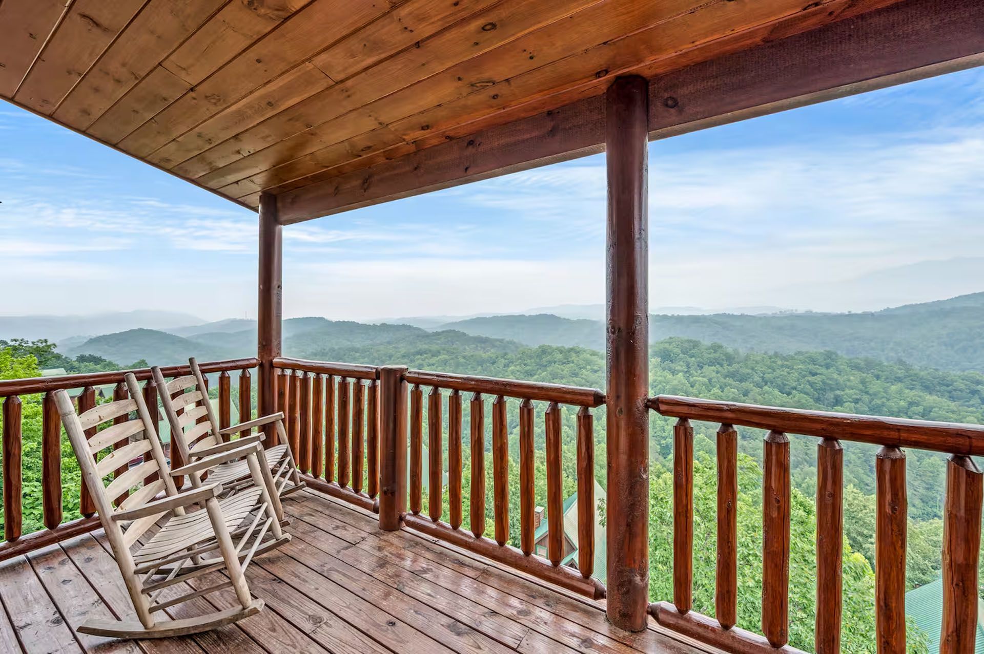 Wooden porch with rocking chairs overlooking a lush, green mountain range under a blue sky.