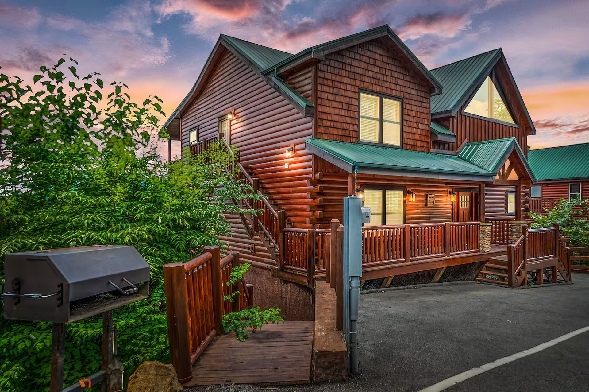 Log cabin with wooden exterior, green roof, and outdoor grill at dusk.