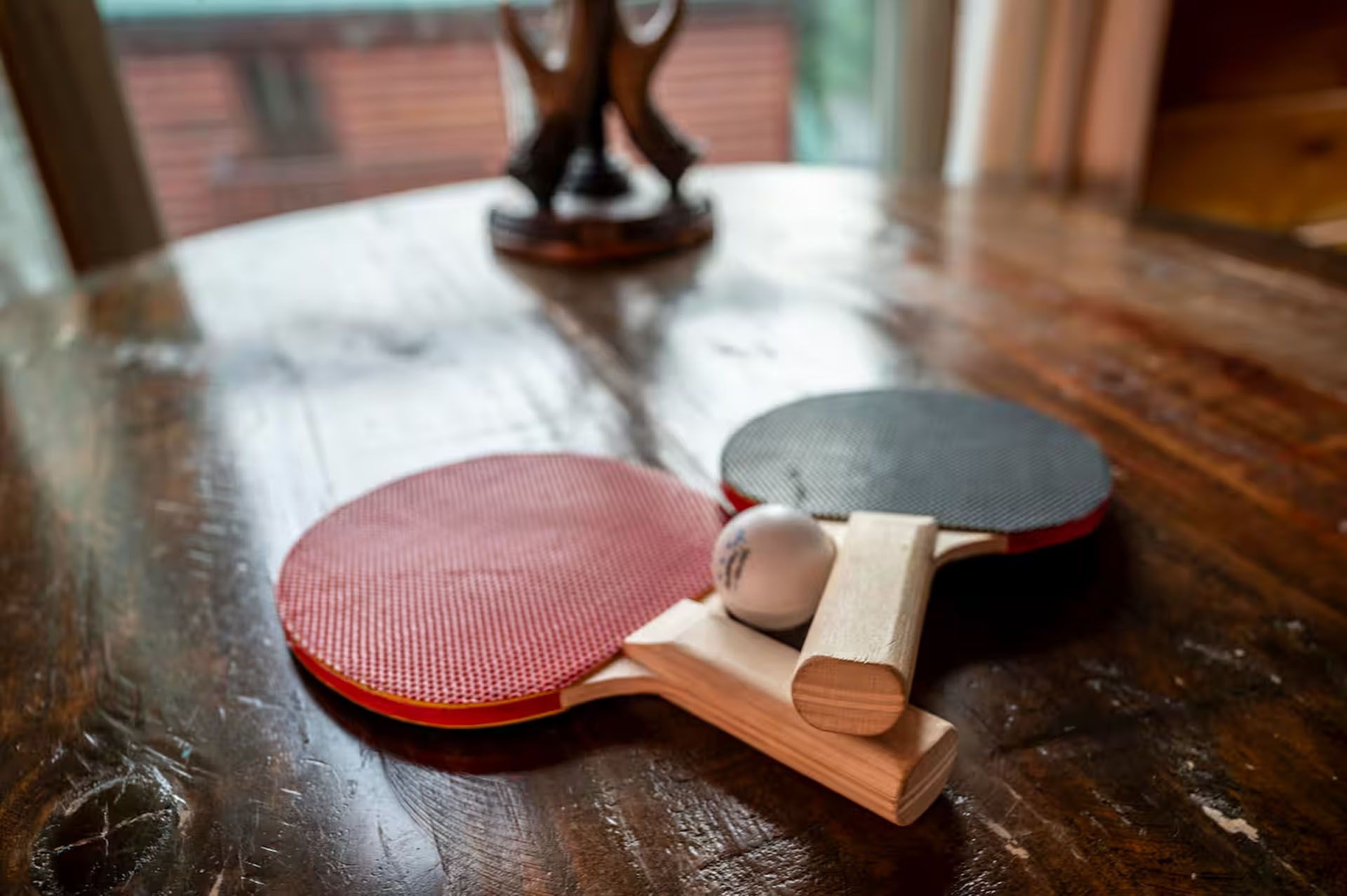 Ping pong paddles and ball on a wooden table with a decorative wooden item in the background.