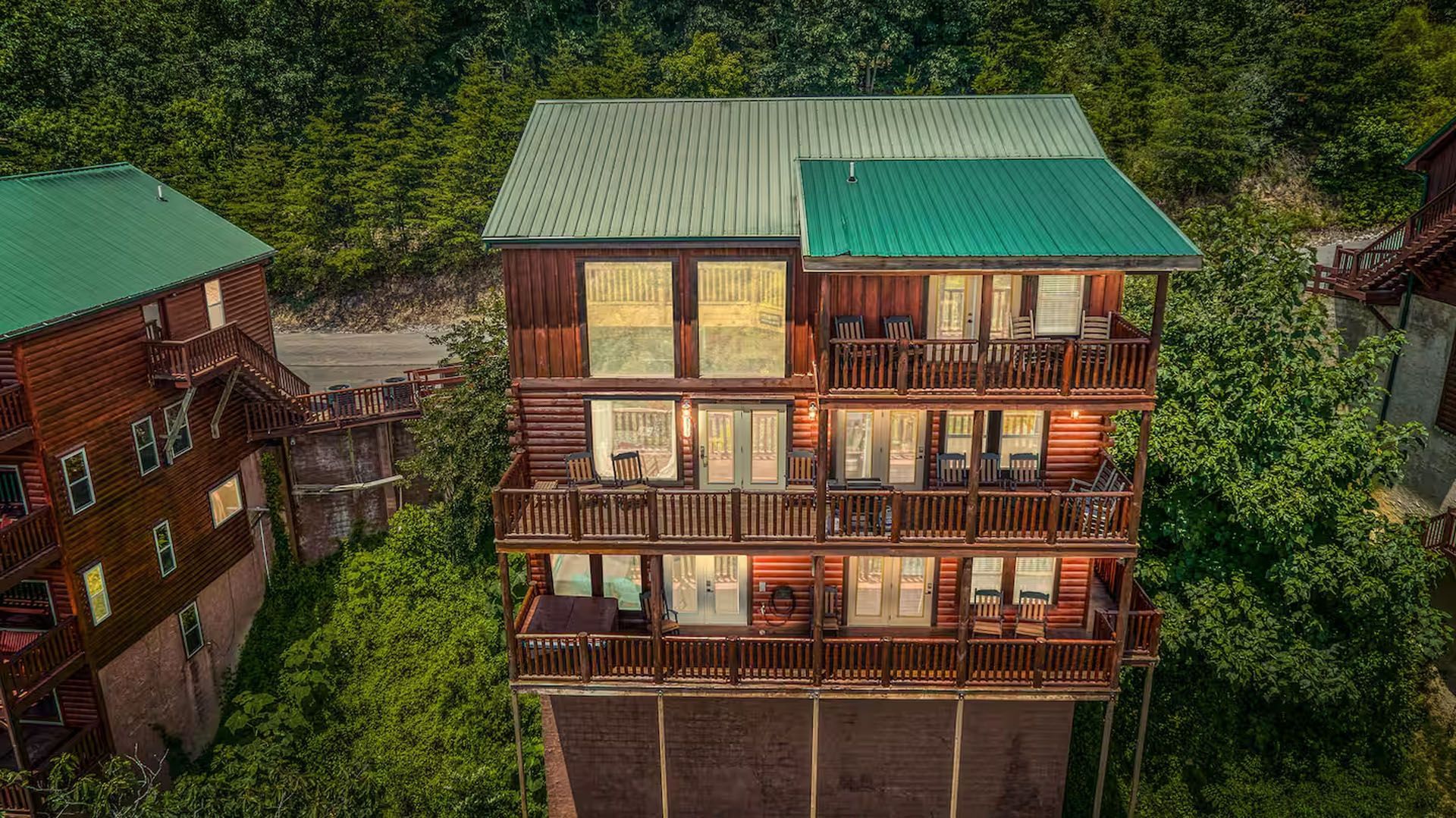 Multi-story wooden cabin nestled in green foliage, with balconies and teal roof.