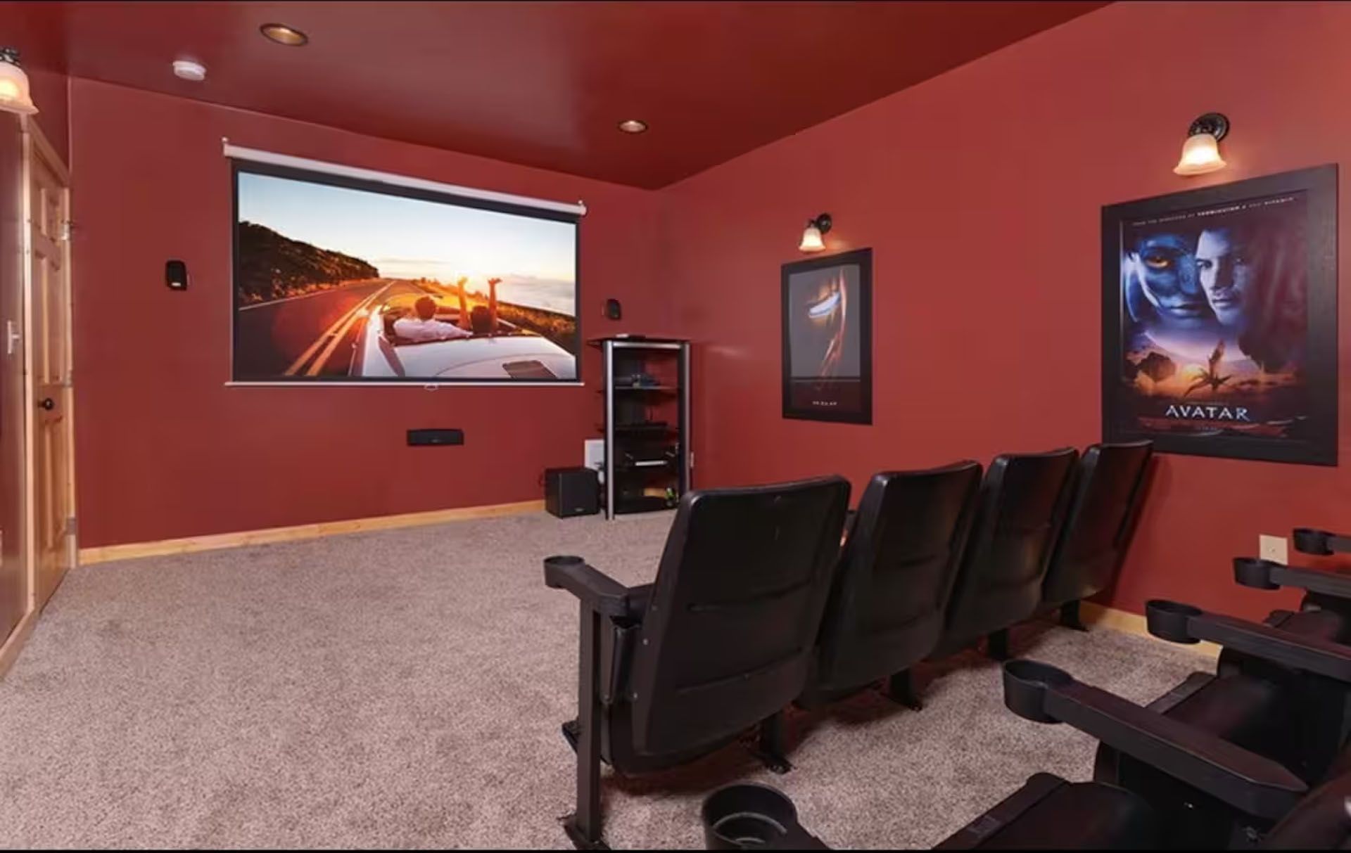 Home theater with rows of black seats, screen showing sunset, red walls, carpet.