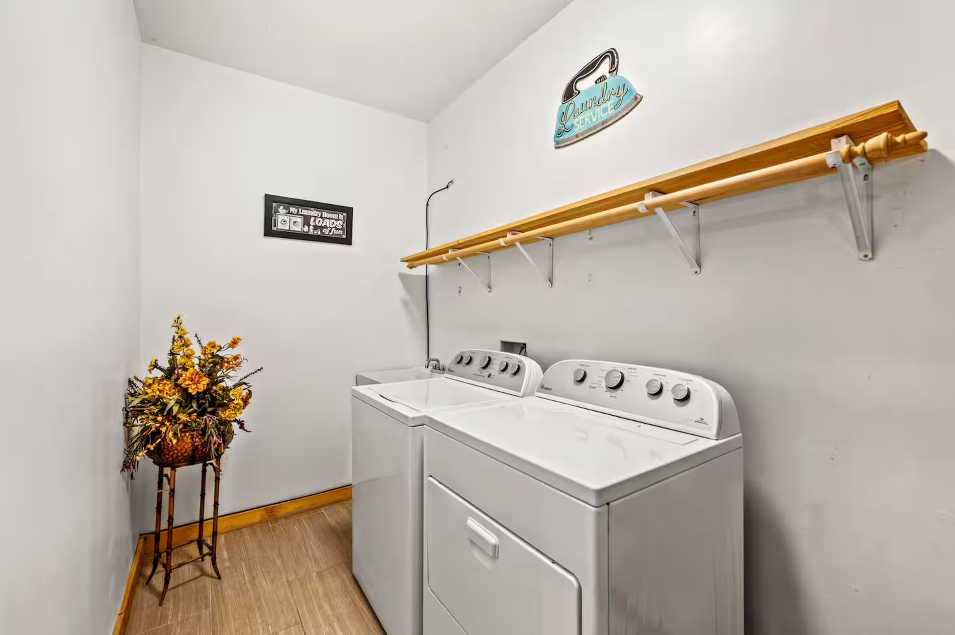 Laundry room with white machines, wood shelving, floral arrangement, and wall decor.