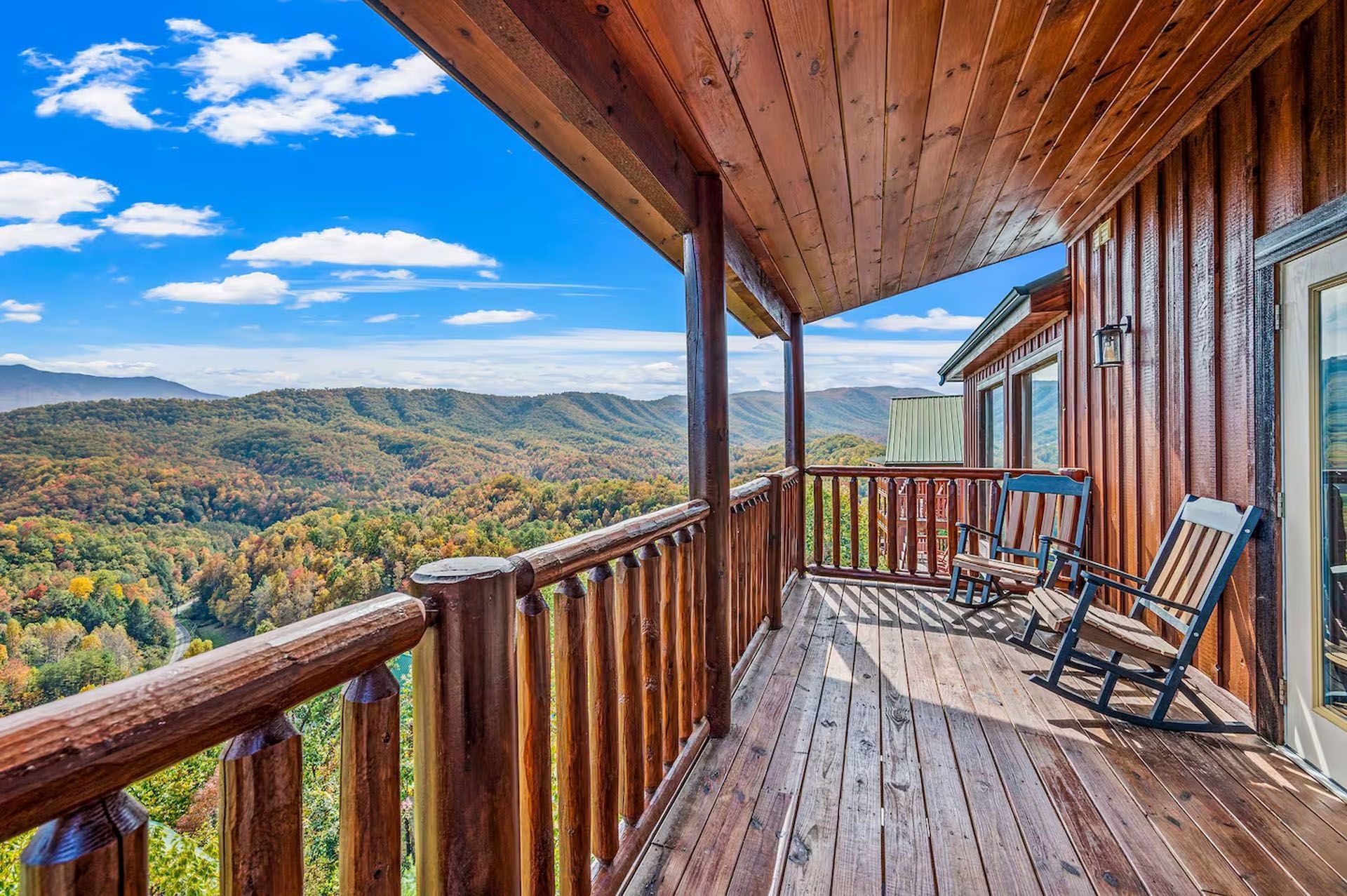 Wooden cabin balcony with rocking chairs, overlooking a mountain range with fall foliage.