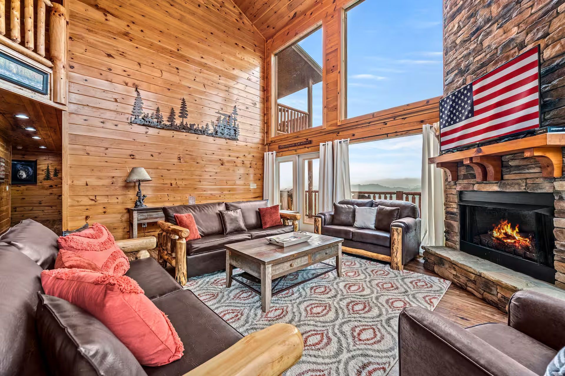 Cozy cabin living room with wood paneling, fireplace, leather furniture, and large windows with a mountain view.