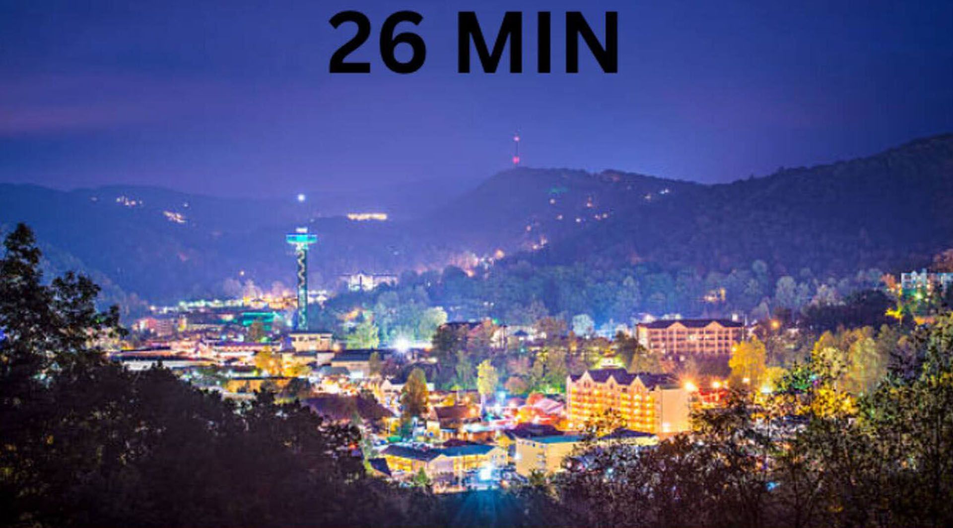 Night view of Gatlinburg, Tennessee, with city lights, mountains, and an observation tower.