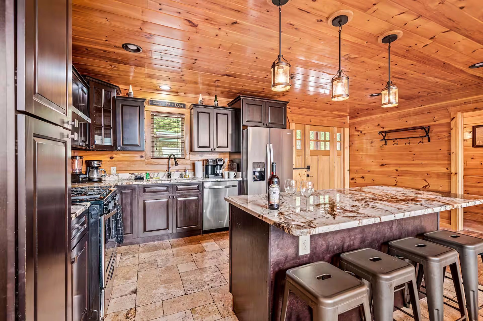 Cabin kitchen with wood paneling, dark cabinets, island with stools, stainless steel appliances.